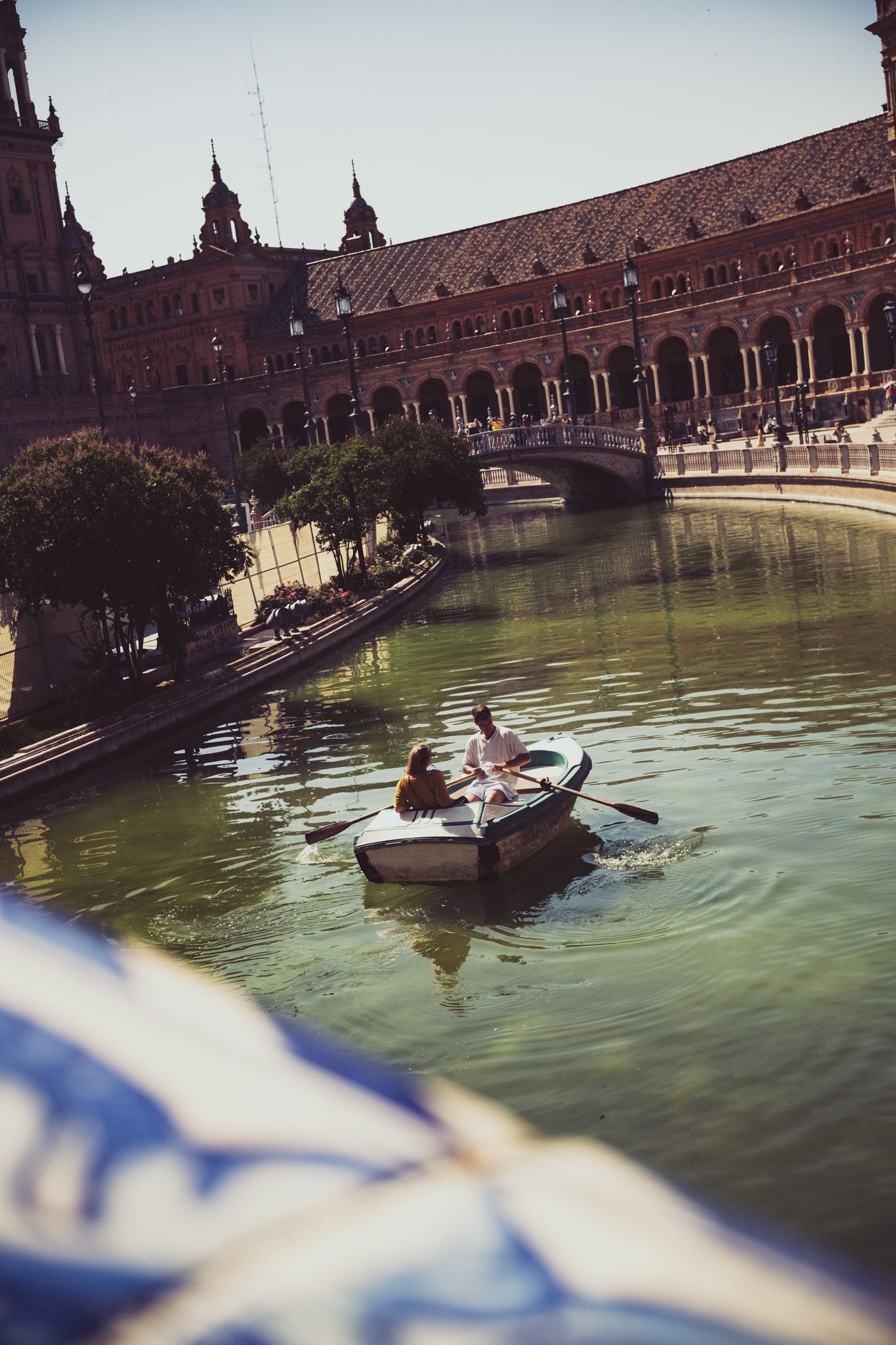 People rowing a boat on the canal at Plaza de Espana Seville Spain with grand building behind.