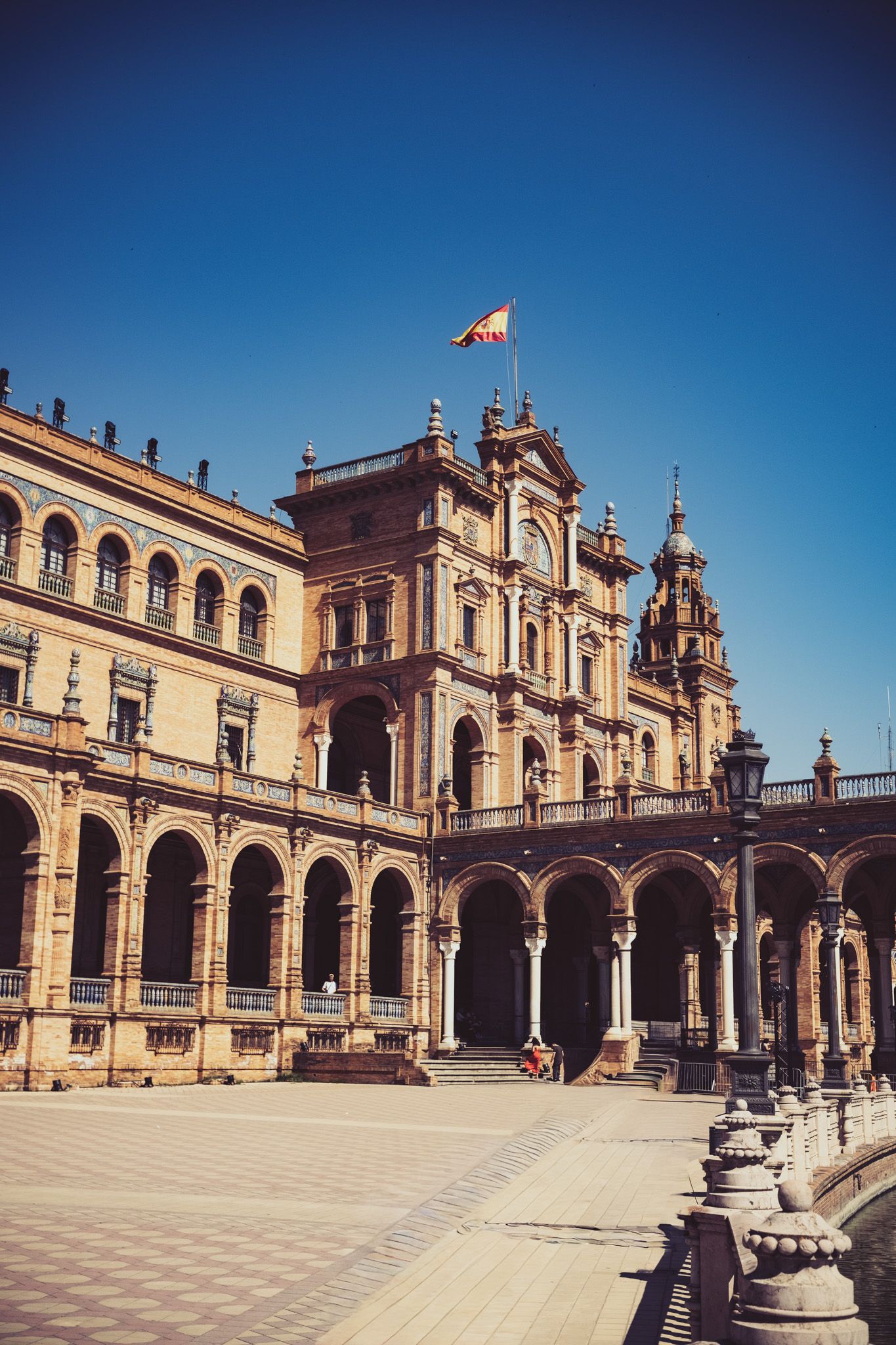 Grand central building of Plaza de Espana Seville Spain with Spanish flag flying under deep blue sky.