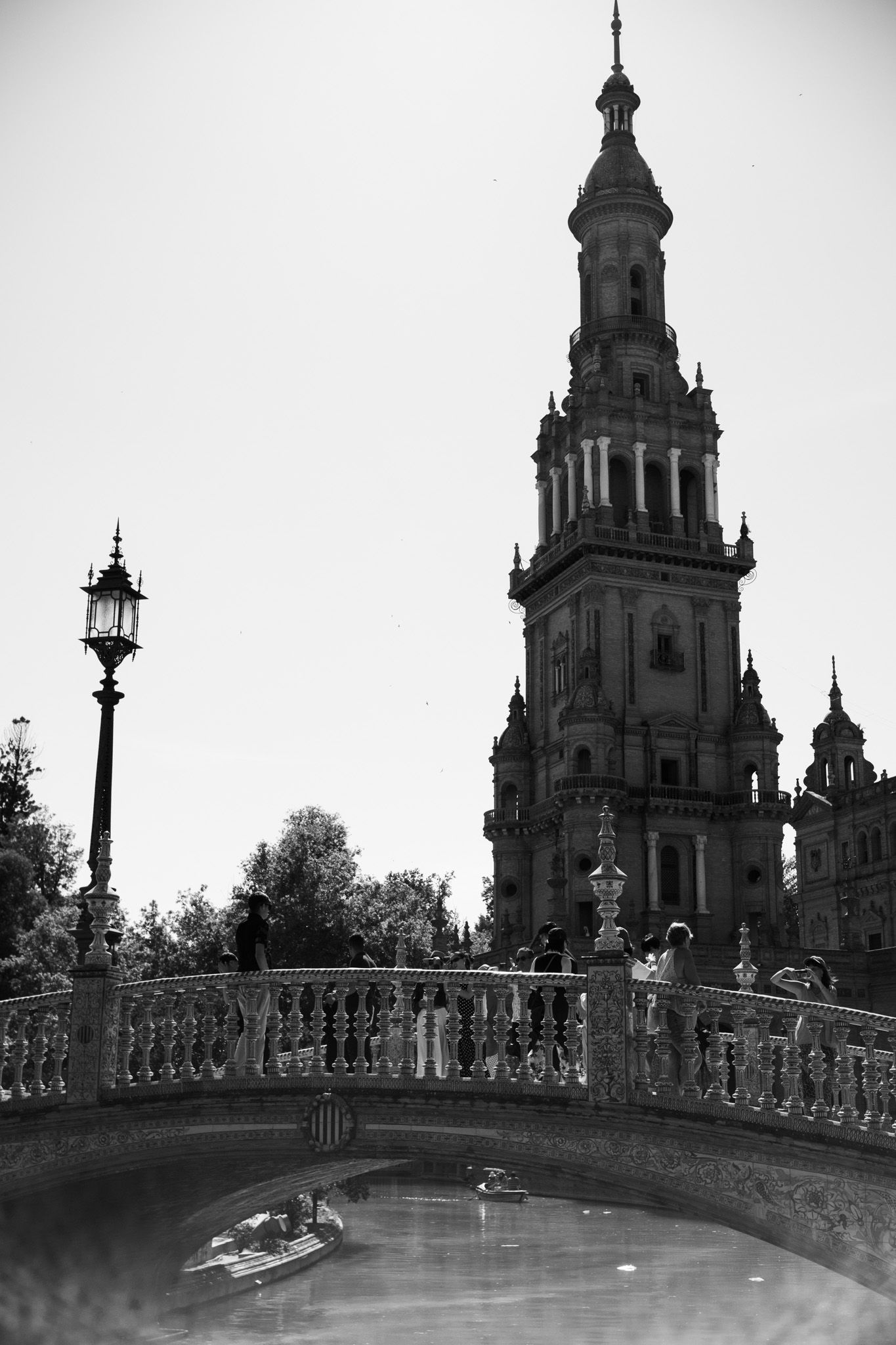 Black and white photo of Plaza de España tower and ornate bridge over canal in Seville, Spain.