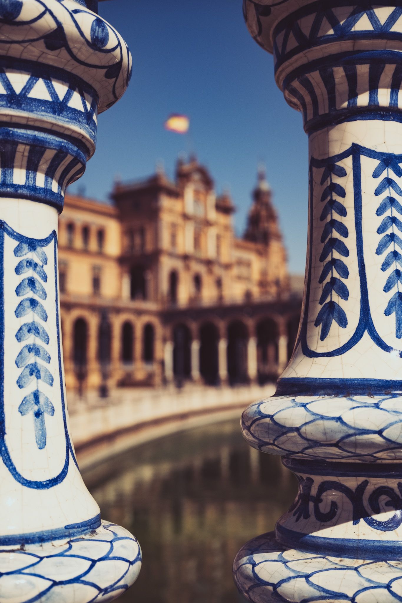 Ornate blue and white ceramic tile balustrade columns framing Plaza de España palace and canal in Seville, Spain.