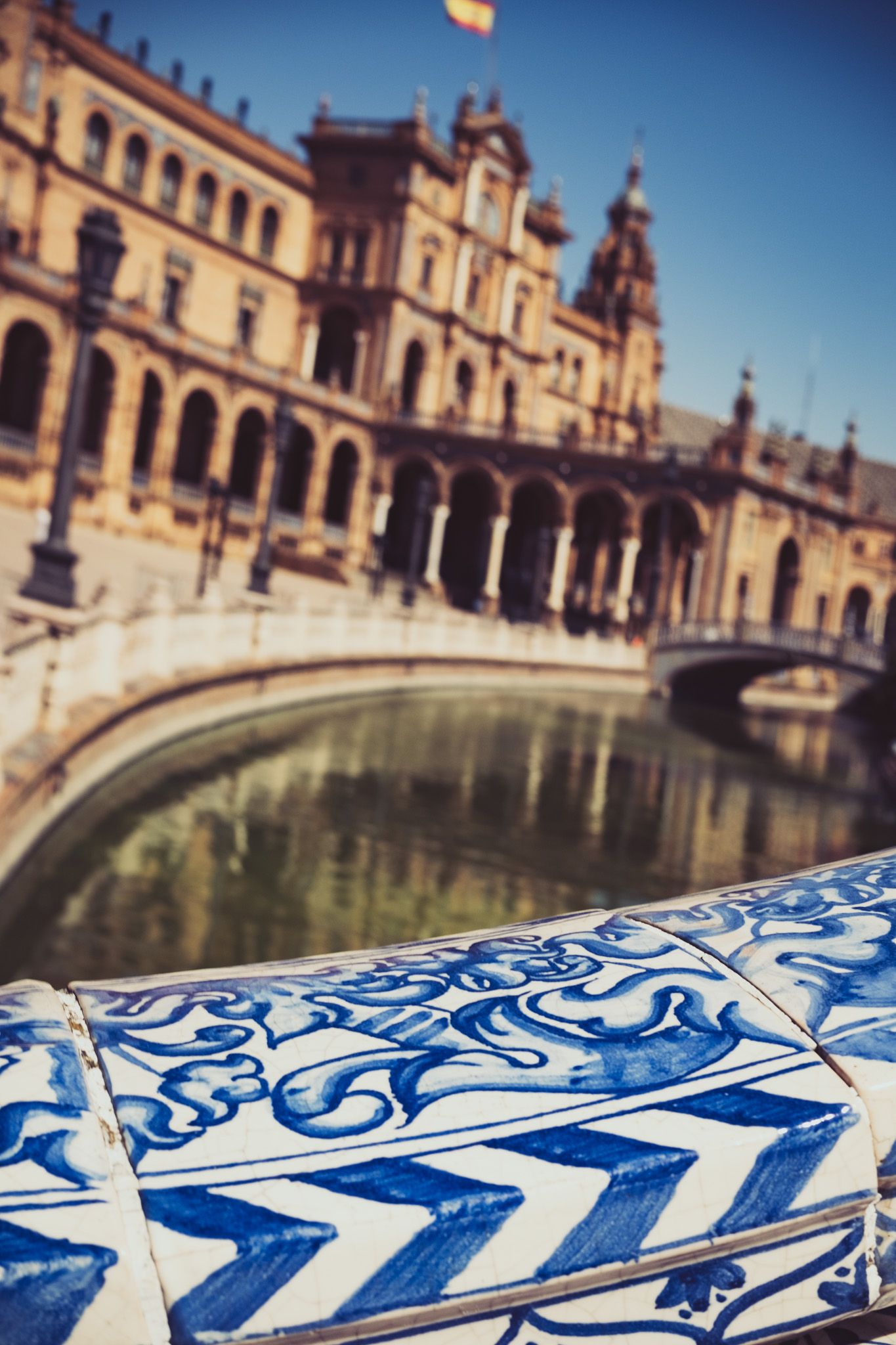 Blue and white azulejo ceramic tile detail at Plaza de España with canal and palace in background, Seville.