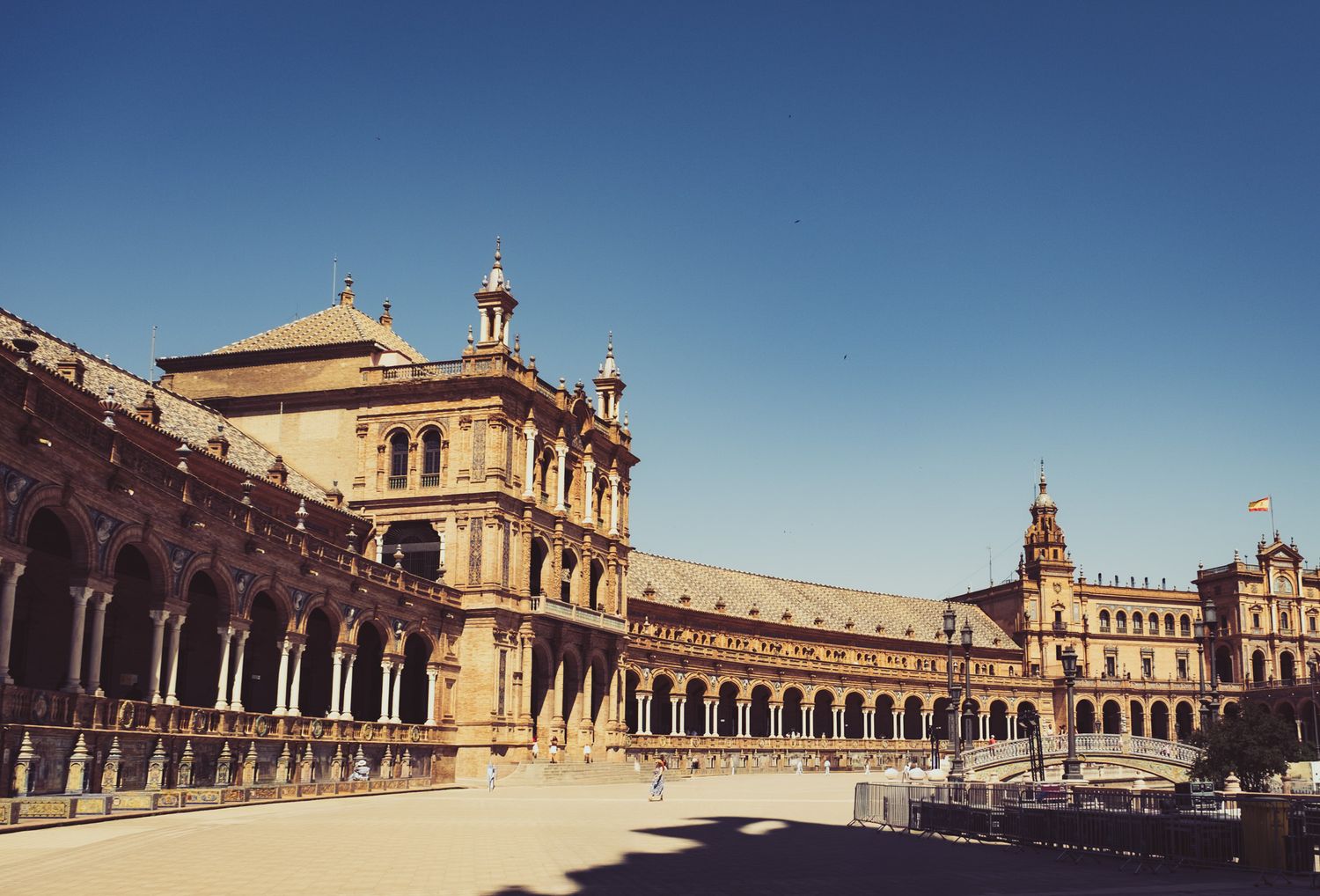 Wide view of the grand semicircular Plaza de España palace with arched colonnades under clear blue sky in Seville.