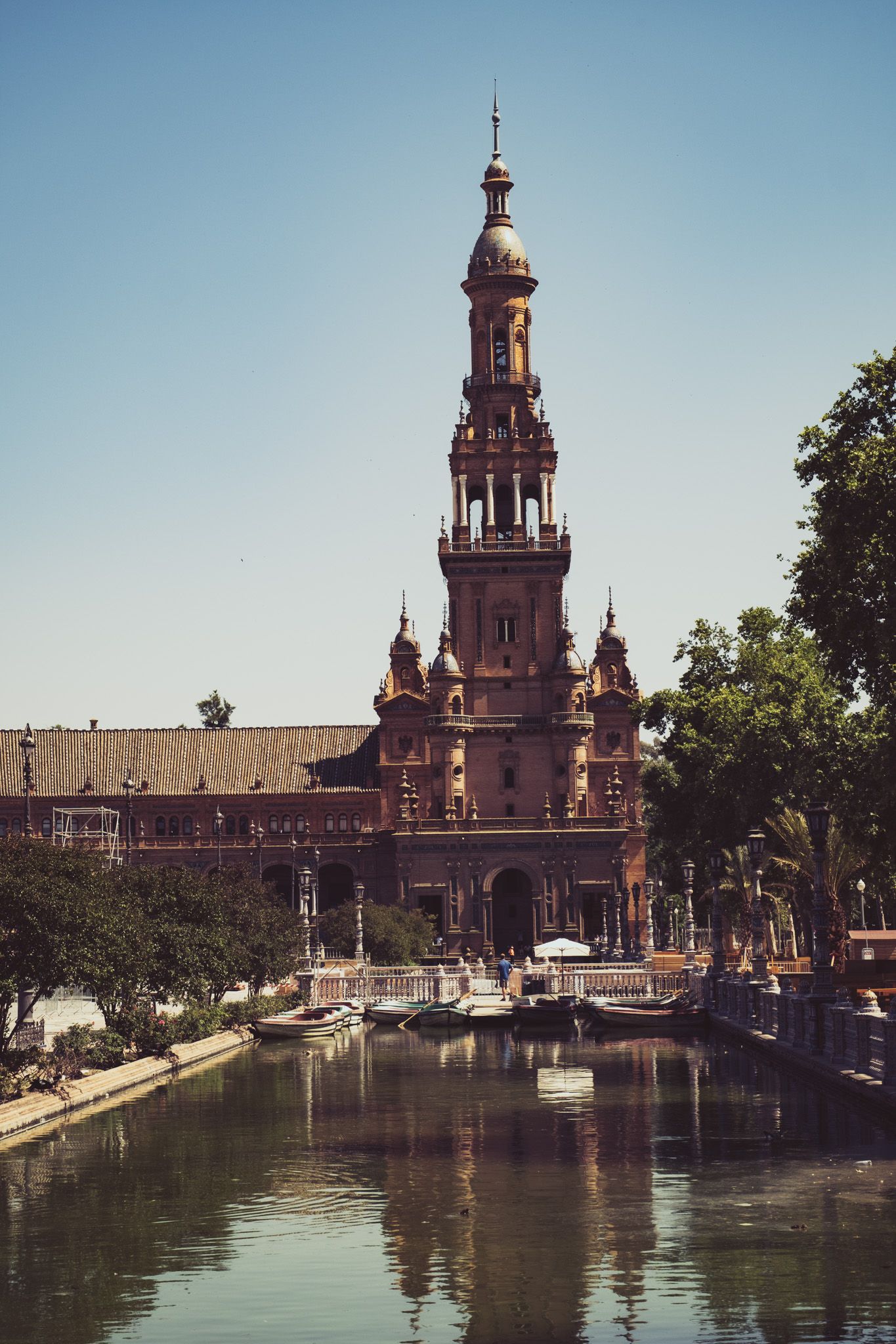 Iconic Plaza de España tower reflected in the canal, Seville, Spain, under a clear blue sky.