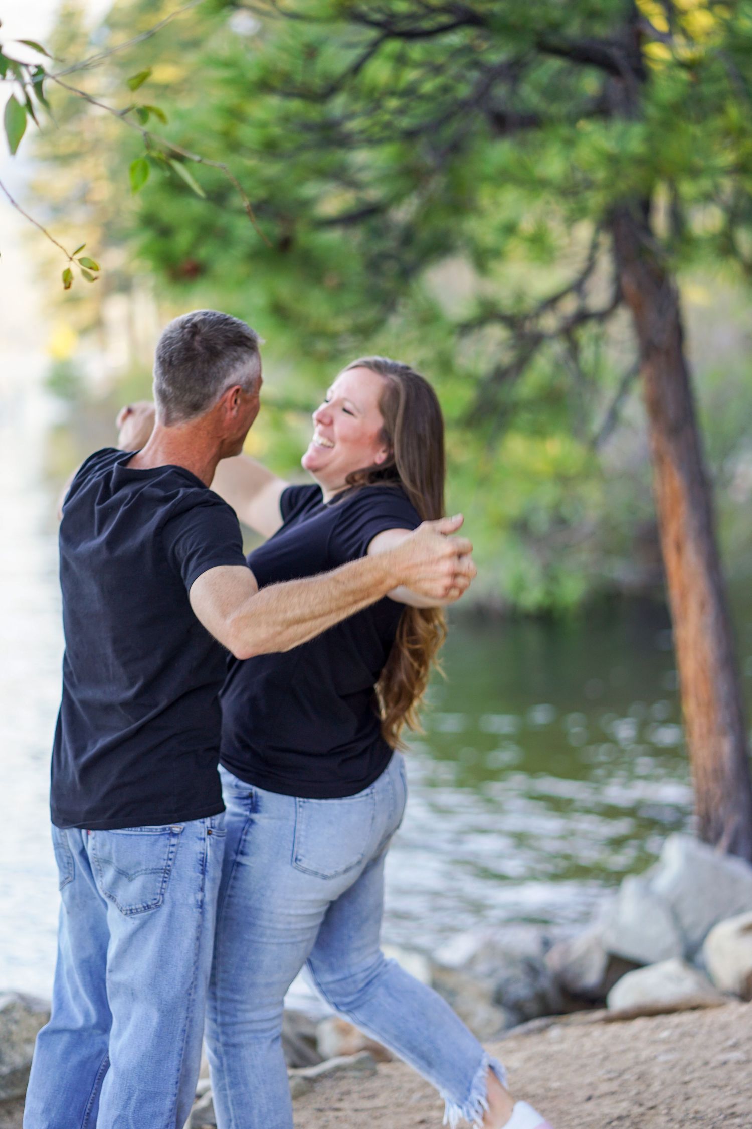 Couple enjoying a romantic moment by lake with trees in background.