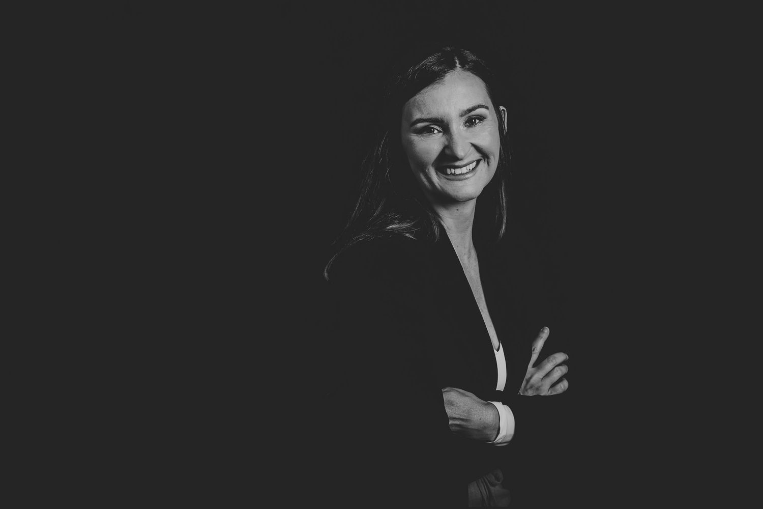 Black and white professional portrait of a smiling businesswoman with arms crossed against dark background.