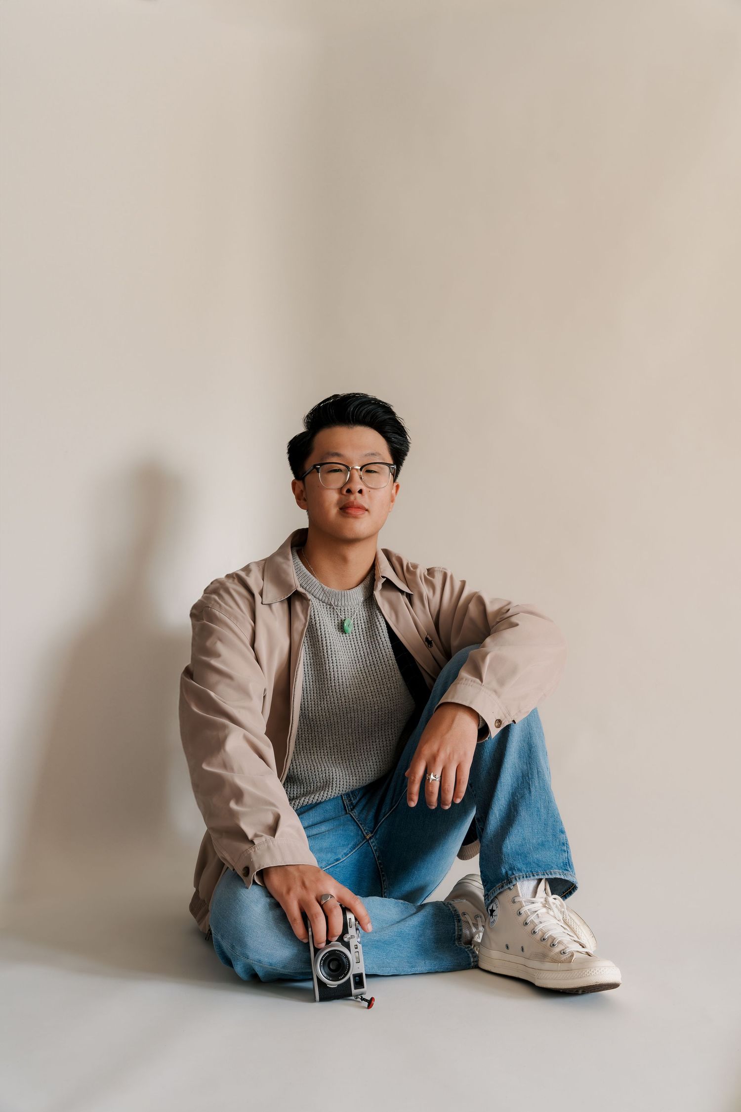 Studio portrait in casual attire against minimalist beige backdrop.