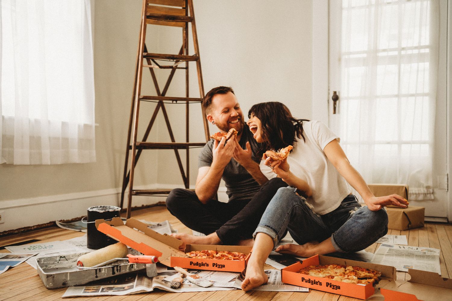 Couple sitting on floor enjoying pizza surrounded by delivery boxes.