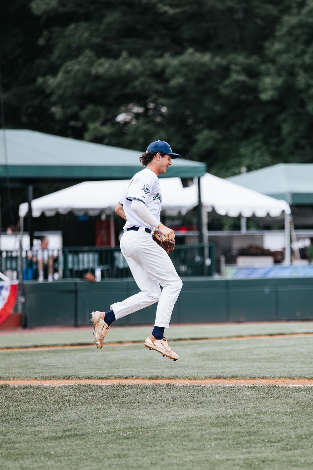 Baseball player in white uniform leaping mid-action on green field during a game.