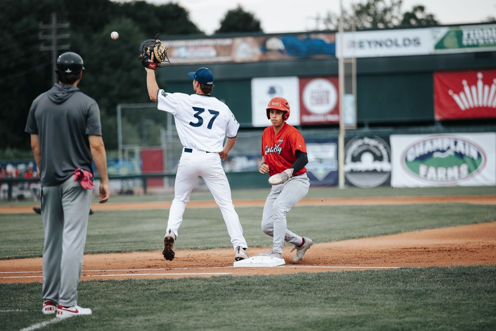 Baseball first baseman catching throw as red-uniformed runner reaches base during competitive game.