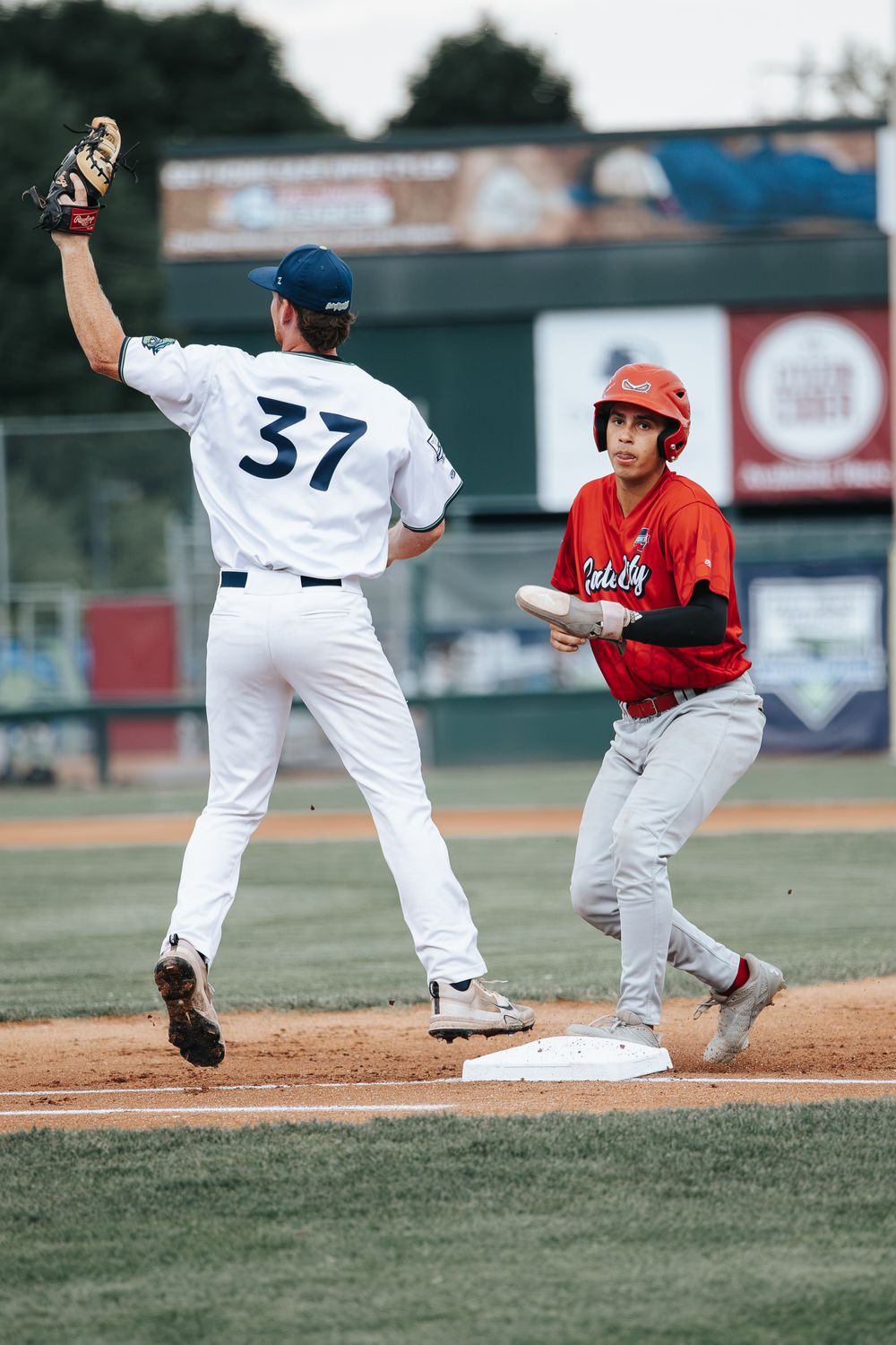 Baseball player #37 catches ball at first base as red-uniformed runner arrives during a competitive game.