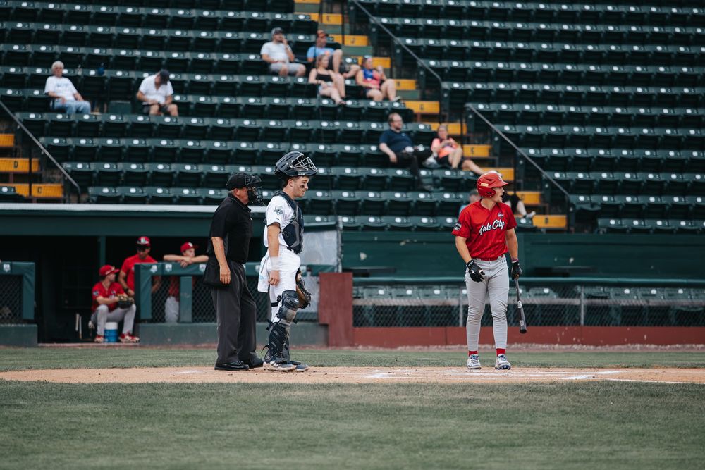 Baseball batter, catcher, and umpire at home plate in stadium with empty green seats behind them.