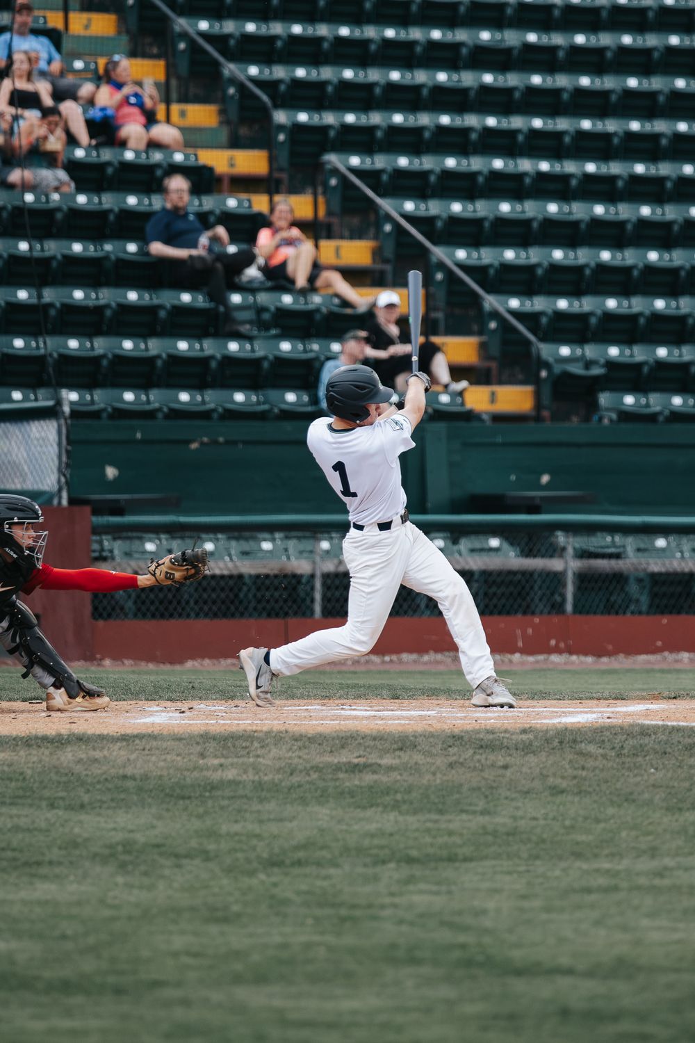 Baseball player in white uniform number 1 swings bat at home plate during a game in a stadium.