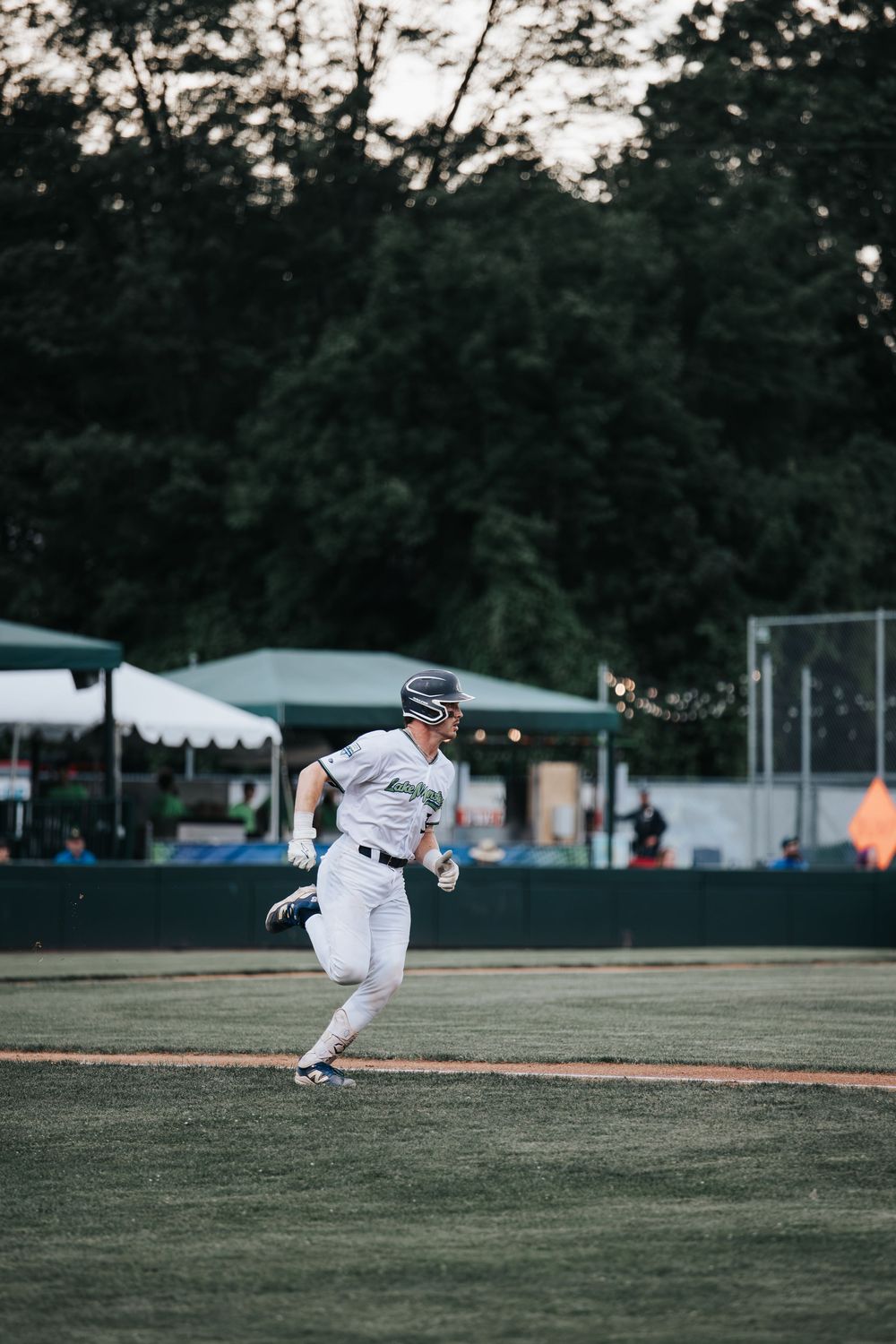 Baseball player in white uniform running the bases on a green field during an evening game.