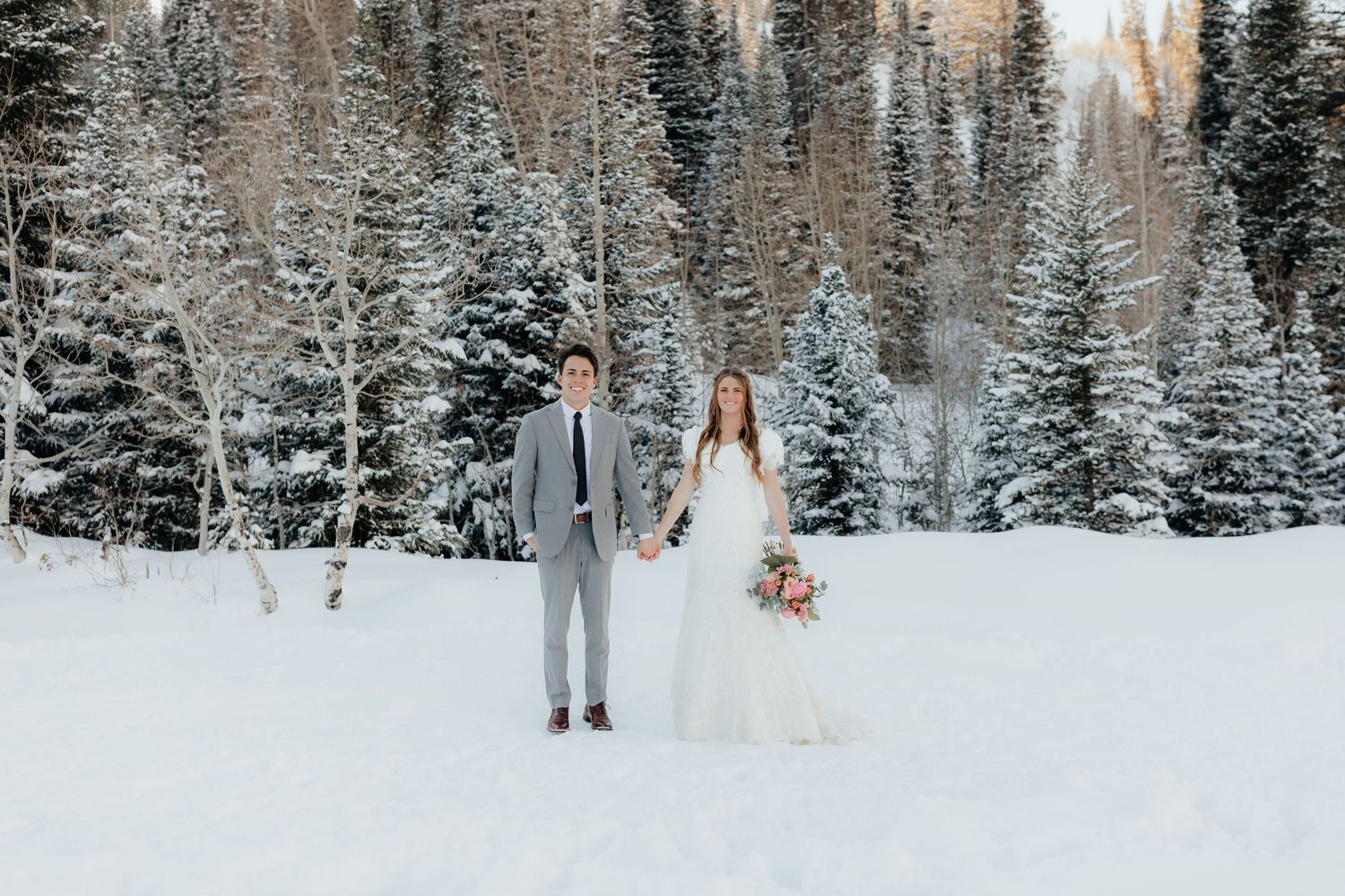 Bride and groom holding hands in winter pine mountains