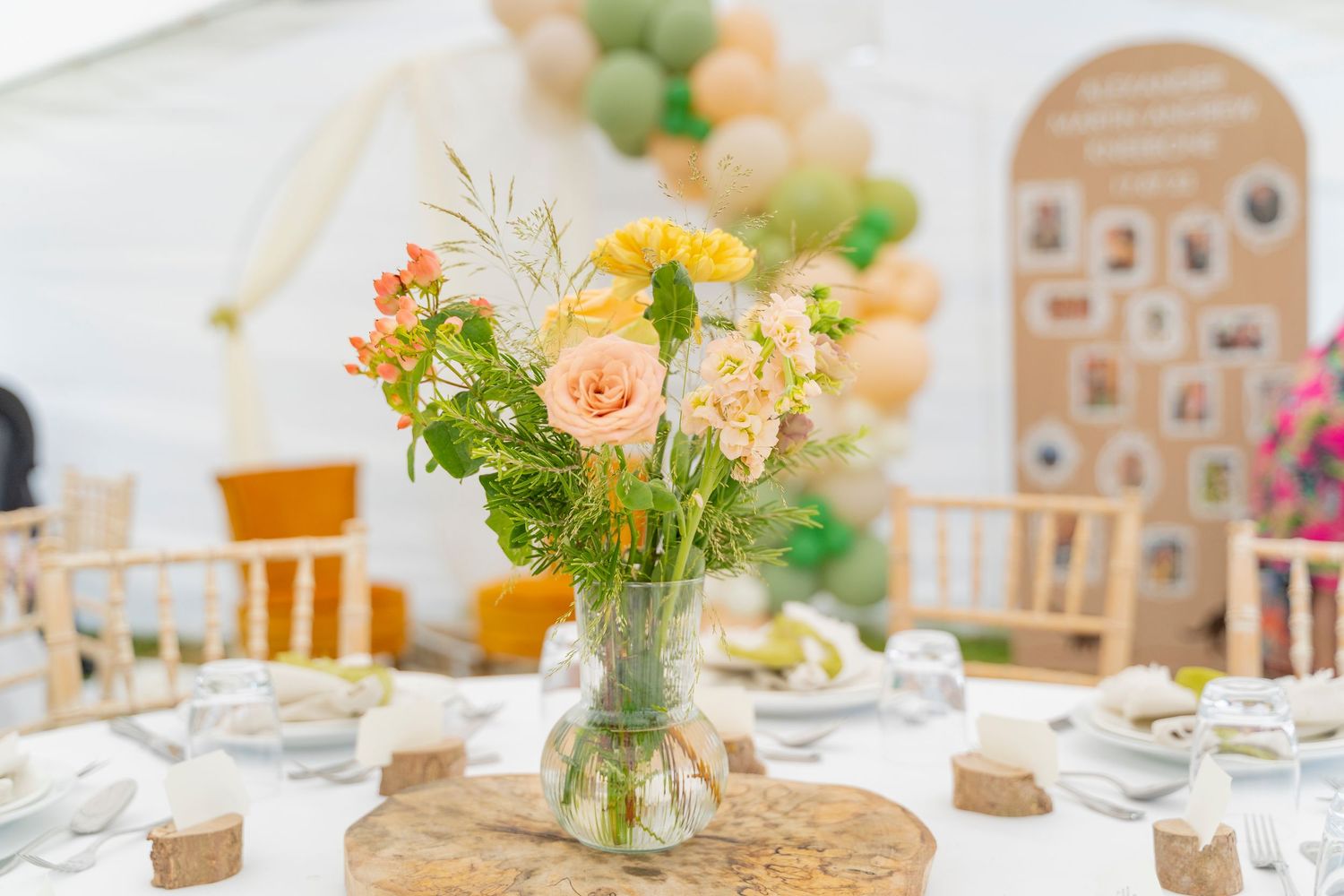 Elegant peach and green floral centerpiece in glass vase on rustic table setting.