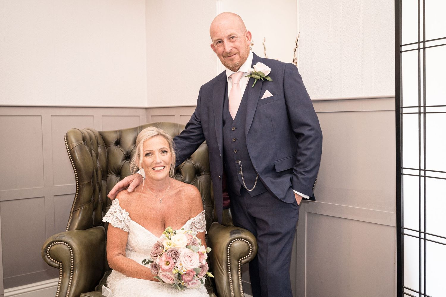 Wedding couple poses in elegant indoor setting with vintage armchair. Elfordleigh Hotel Wedding. Devon Wedding Photography