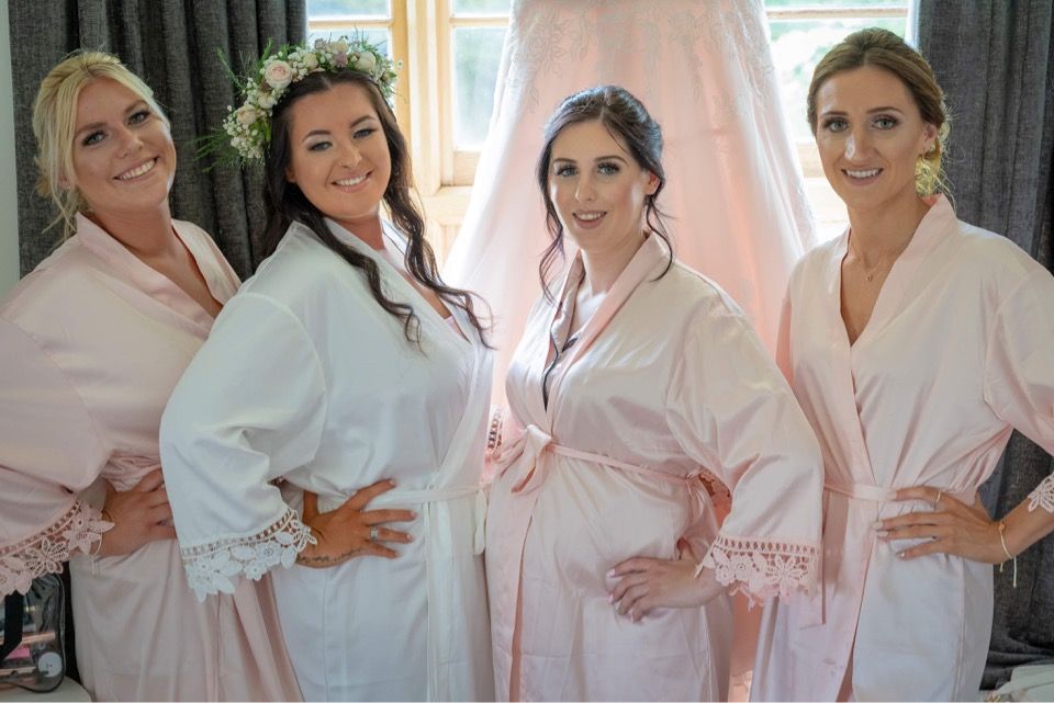 Four women wearing matching white robes pose together indoors.