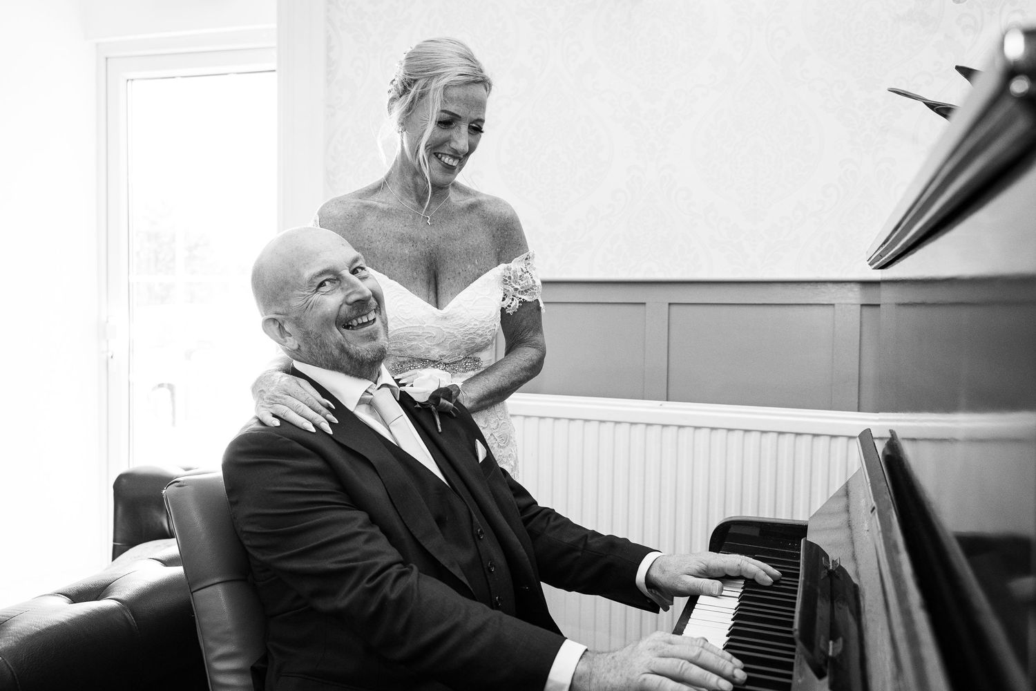 Black and white photo of joyful moment at piano during wedding celebration. Elfordleigh Hotel Wedding. Devon Wedding Photography