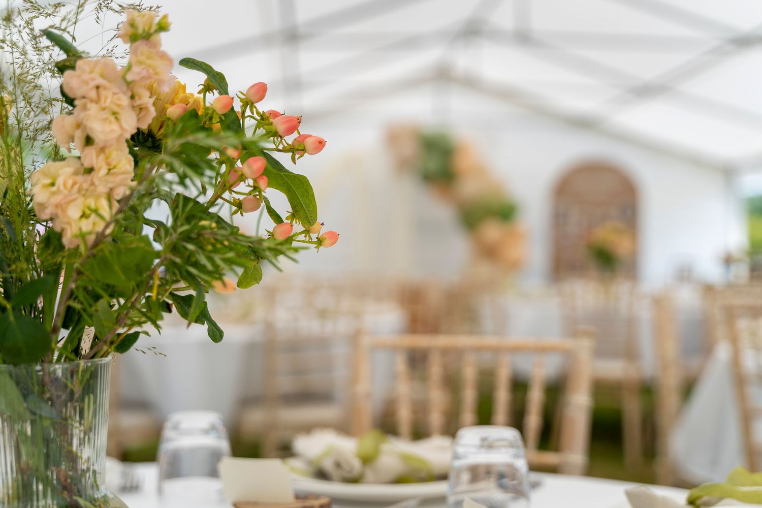 Wedding reception table settings with floral arrangements in marquee tent.