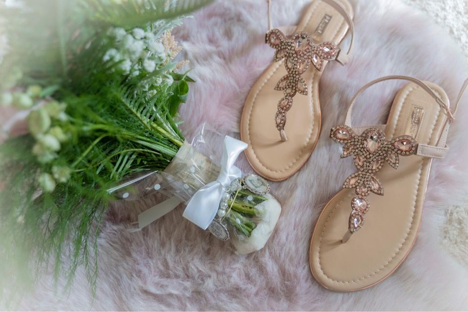 Crystal embellished bridal sandals next to delicate floral arrangement.