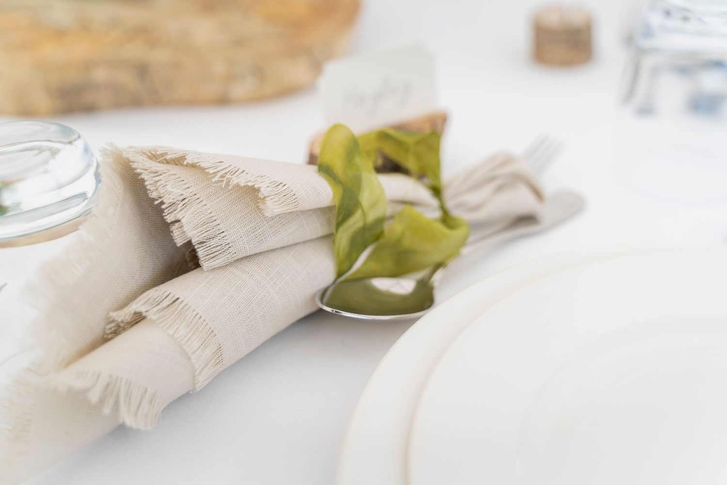 Close-up of rustic table setting with frayed linen napkin and green foliage detail.