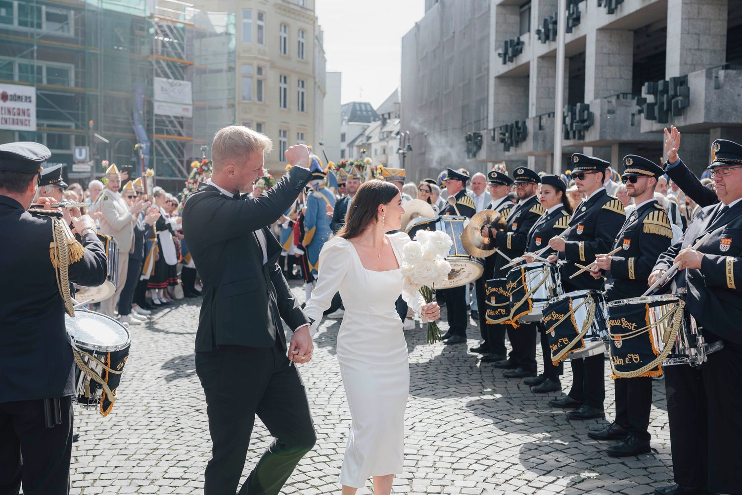 Bride and groom walk through a marching band guard of honor on cobblestone street on their wedding day.