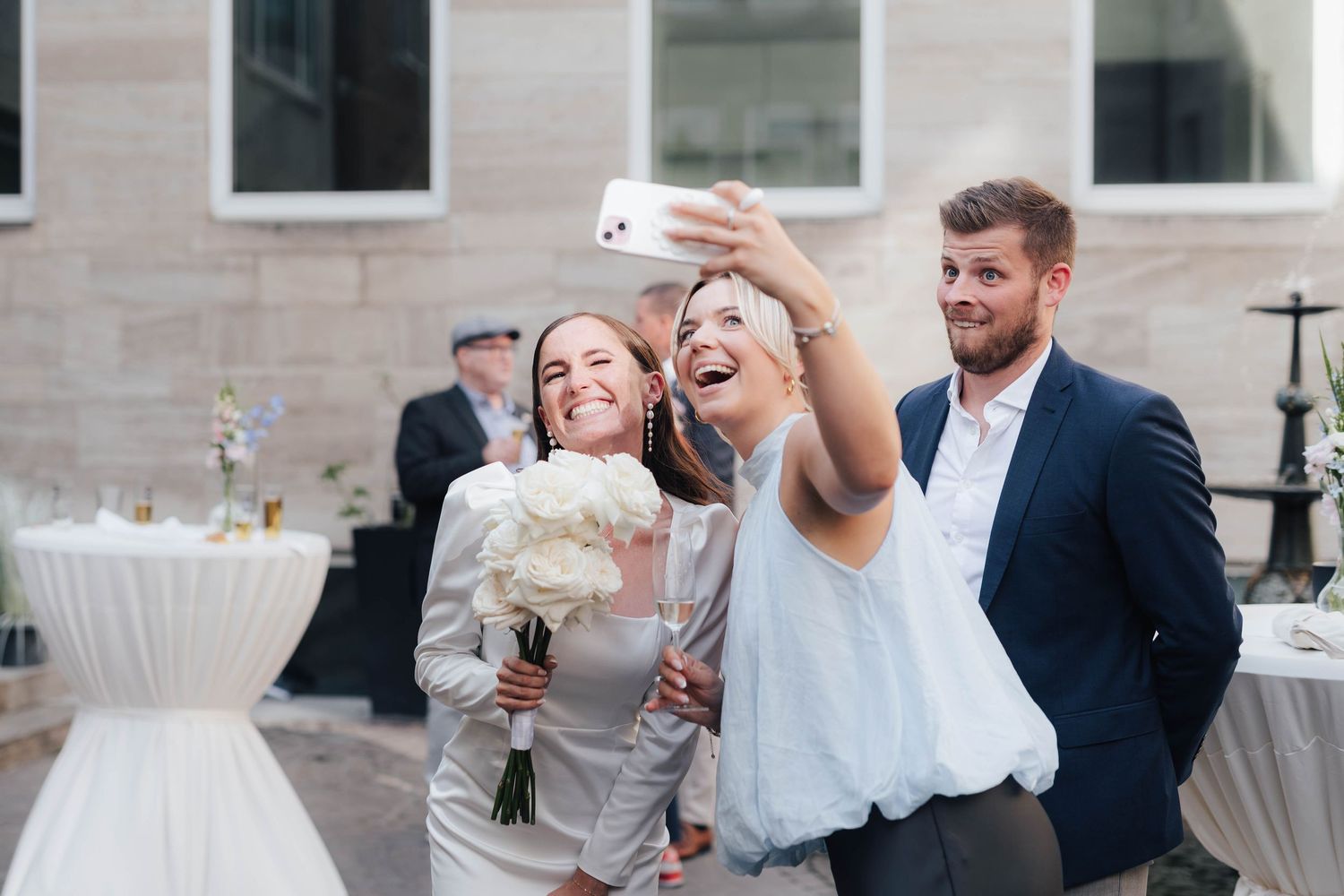 Bride and bridesmaids laughing while taking a selfie at an outdoor wedding reception.