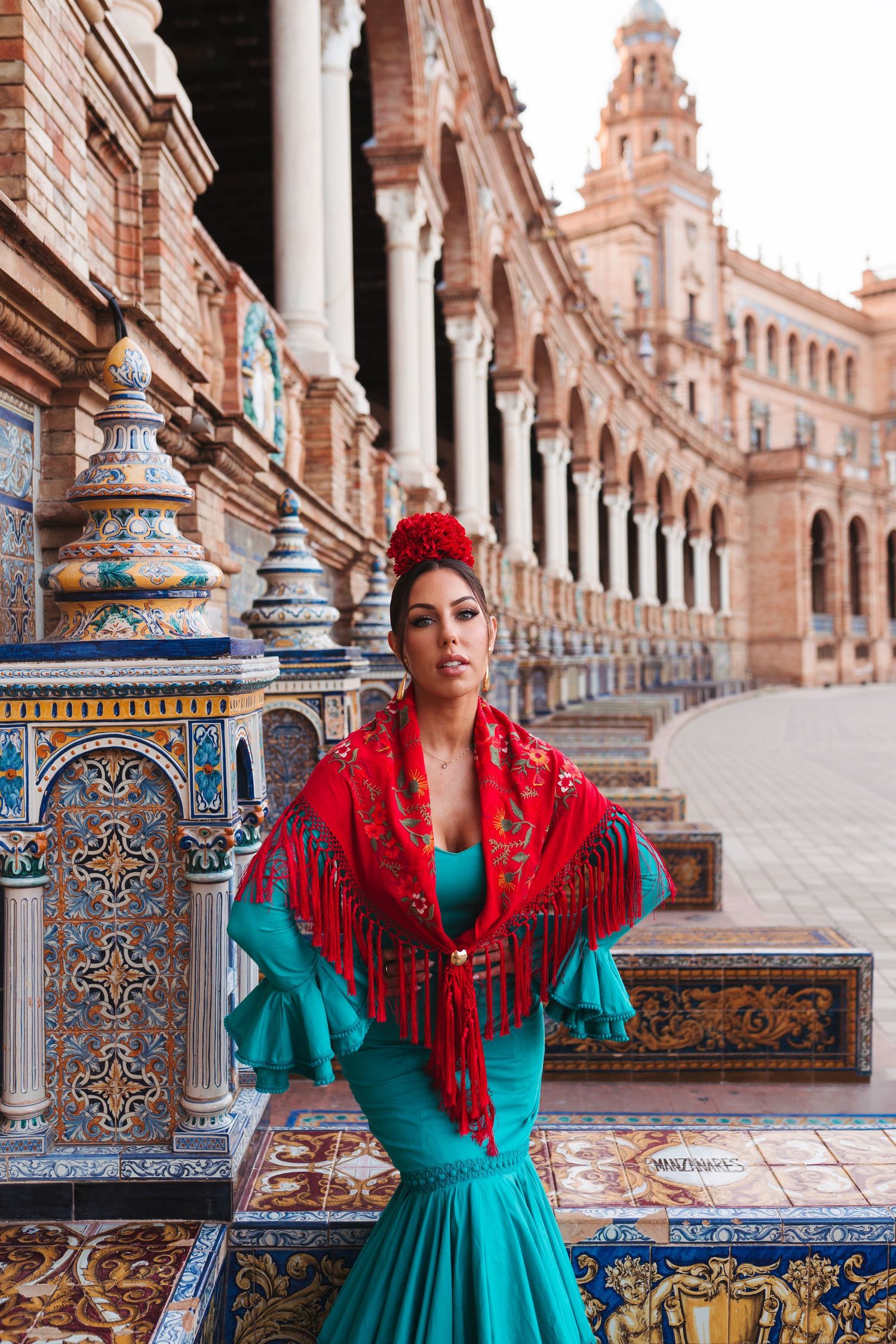 Flamenco dancer in turquoise dress and red shawl poses at Plaza de España, Seville, Spain.