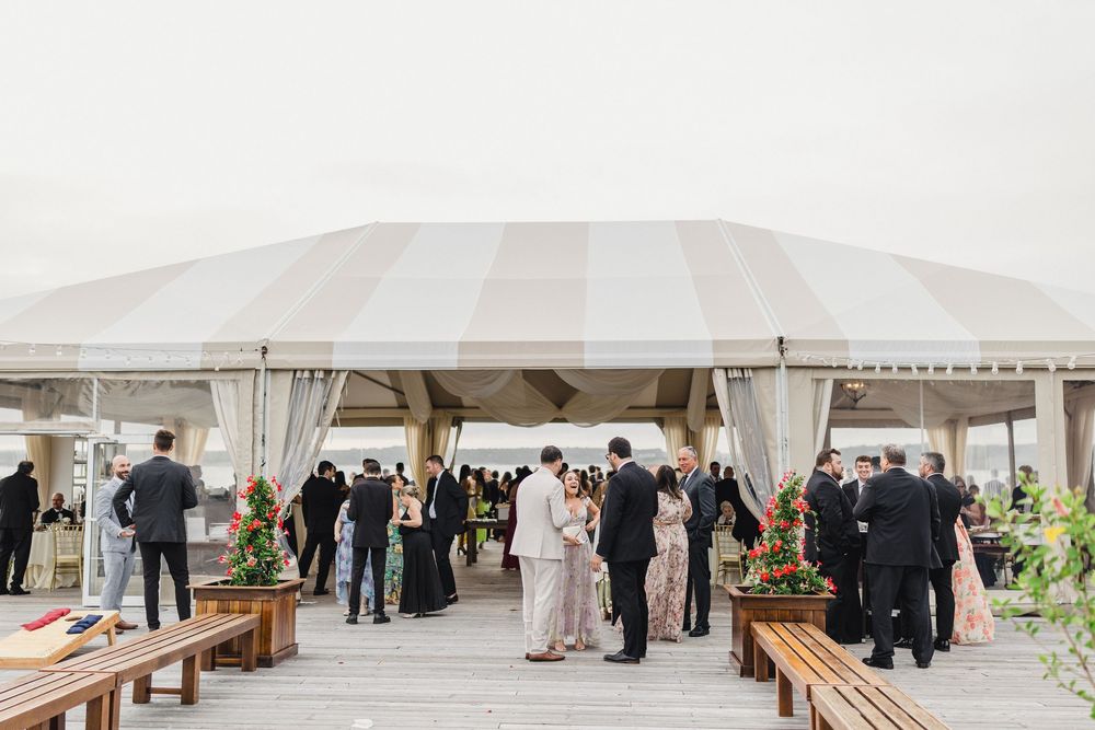 Guests mingle outside a large striped tent at OceanCliff Hotel in Newport, Rhode Island. Wedding photographer