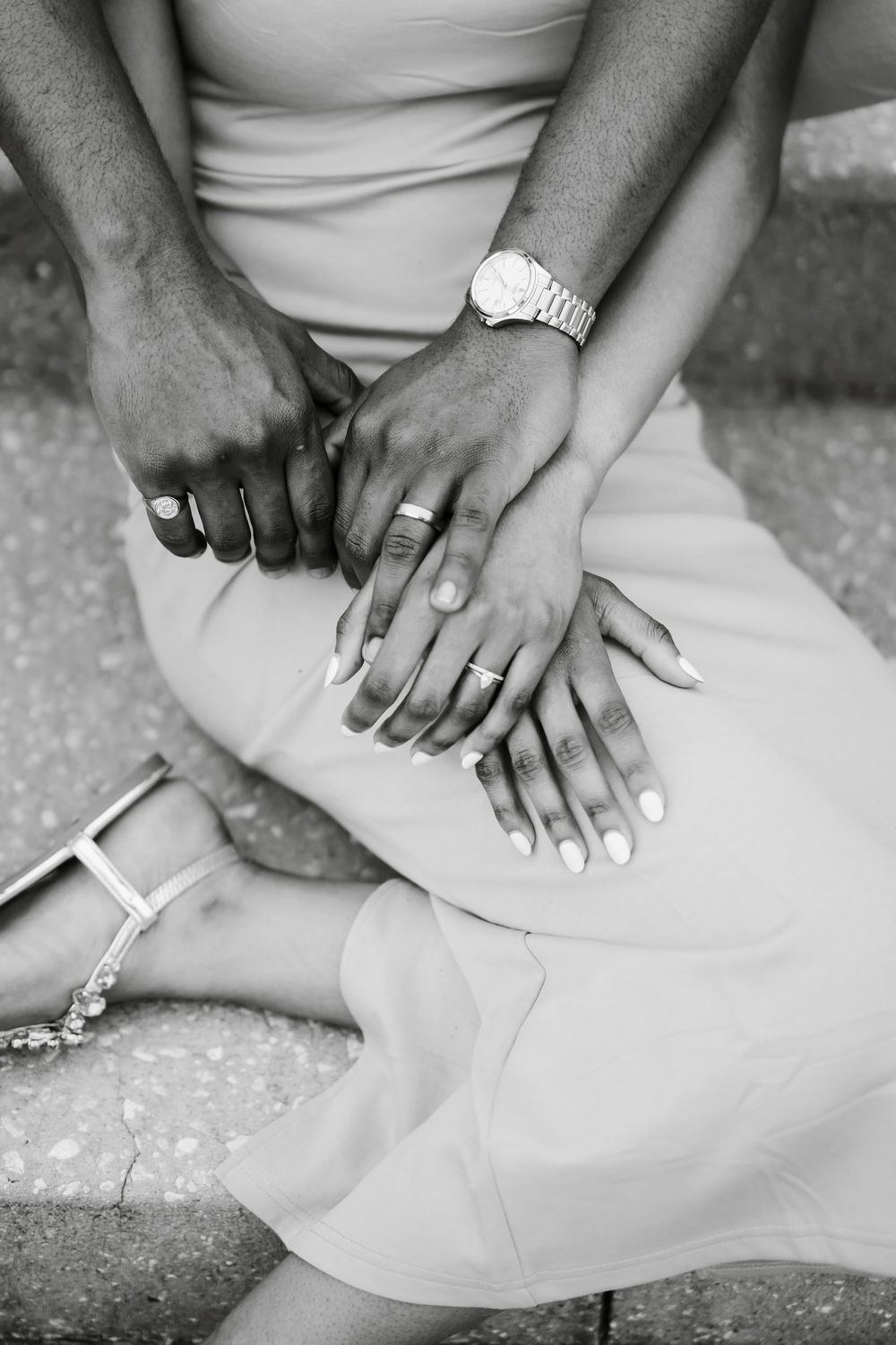 Black and white photo of a couple holding hands, showing wedding rings and a watch, with the woman in a light dress.
