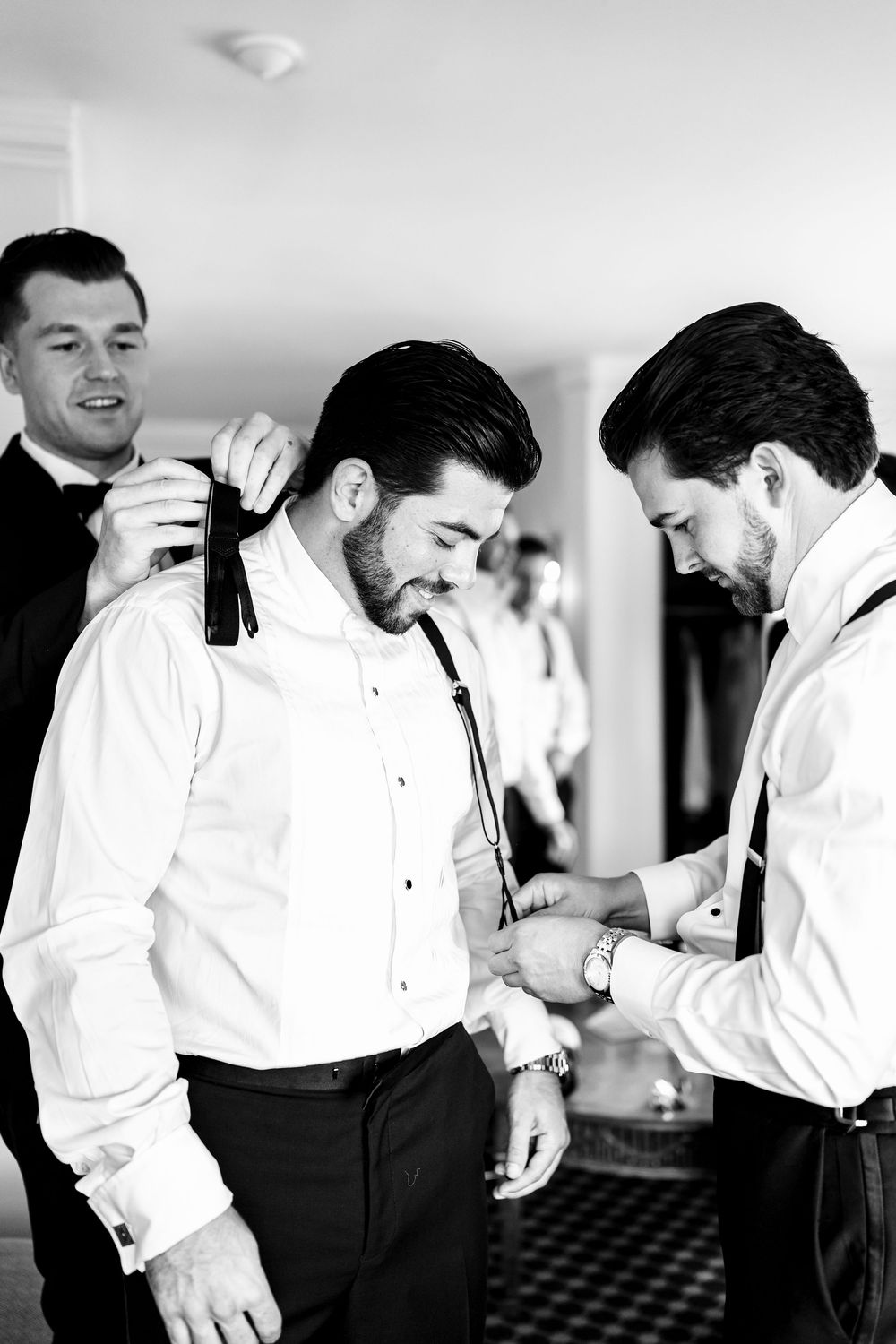 Groomsmen helping groom adjust tie and cufflinks groomsmen before the wedding at OceanCliff Hotel.