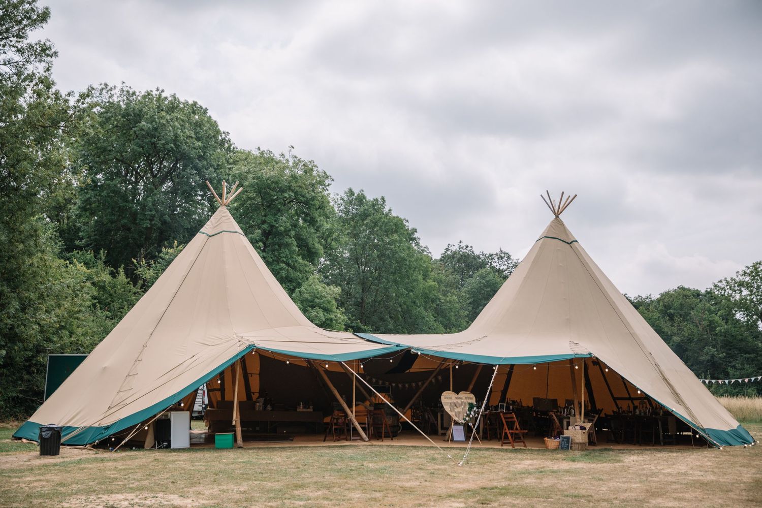 Large beige teepee-style wedding tent setup in a grassy field under cloudy skies.