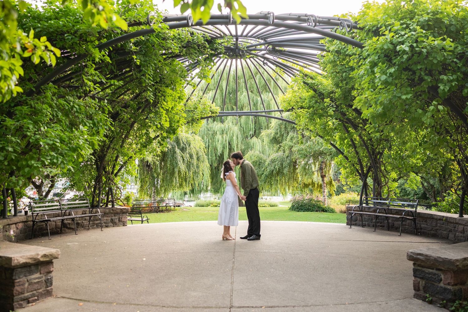 Man proposes on one knee in lush garden with Toronto CN Tower skyline and lake in the background.