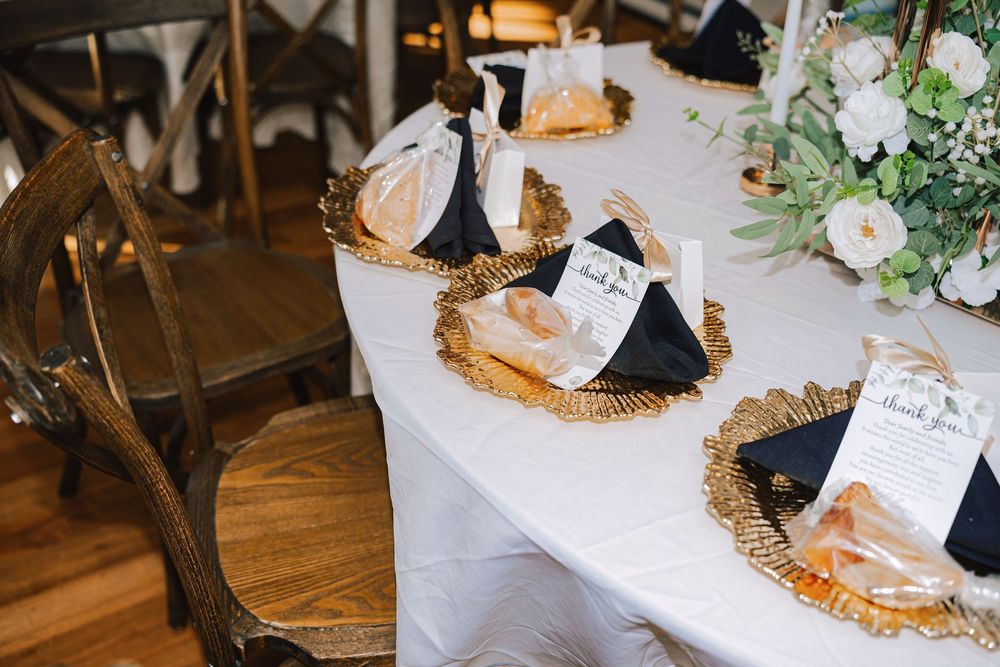 Elegant wedding reception table with gold chargers, navy napkins, and personalized favor bags on white linen.