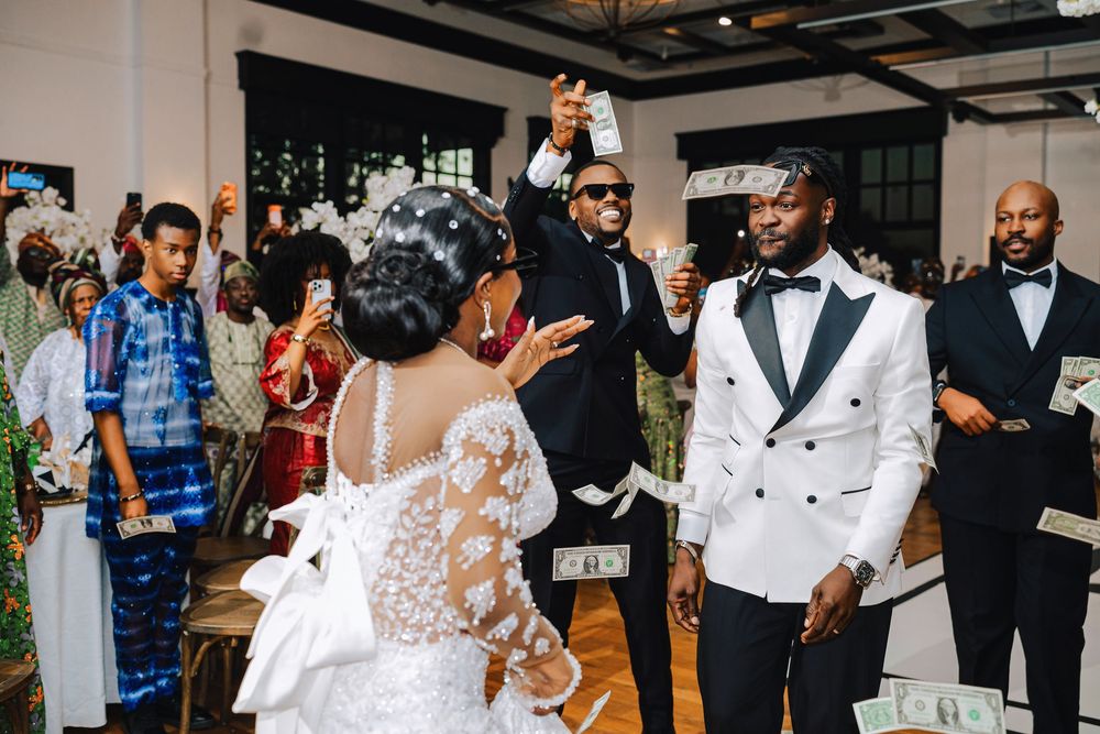 Joyful wedding reception with bride in lace gown, groom in white tuxedo, guests celebrating with money dance tradition.