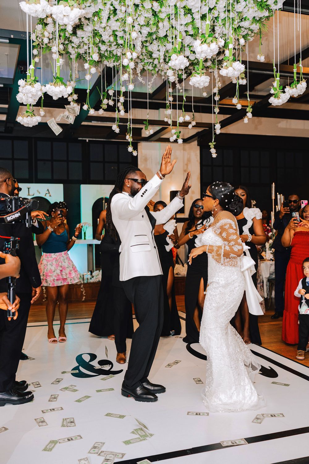 Joyful newlyweds share first dance under hanging floral installation on decorated white dance floor at wedding reception.