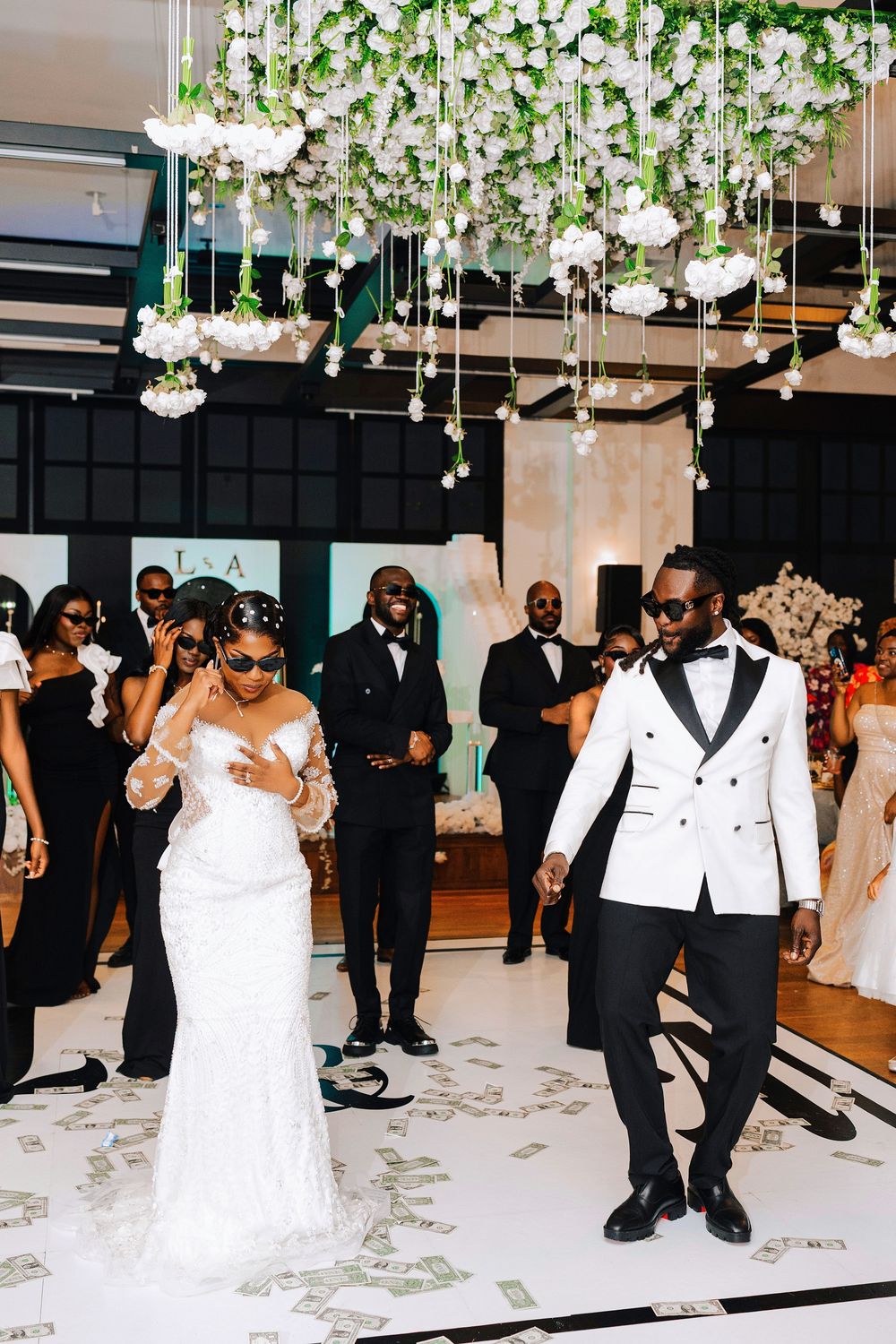 Bride and groom dancing at elegant wedding reception with floral ceiling installation and guests in formal attire.