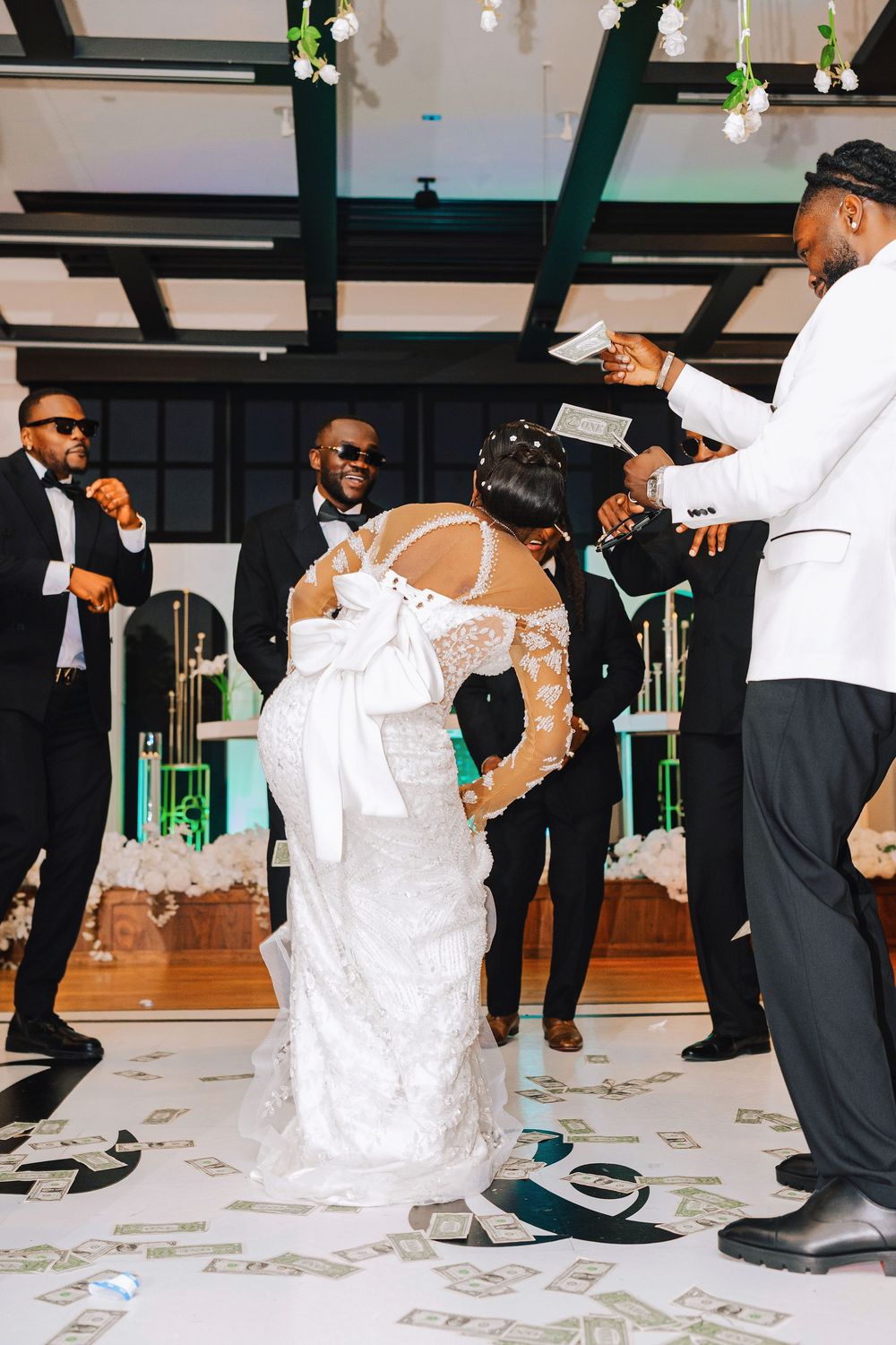 Bride in lace wedding dress being sprayed with money during traditional wedding reception dance.