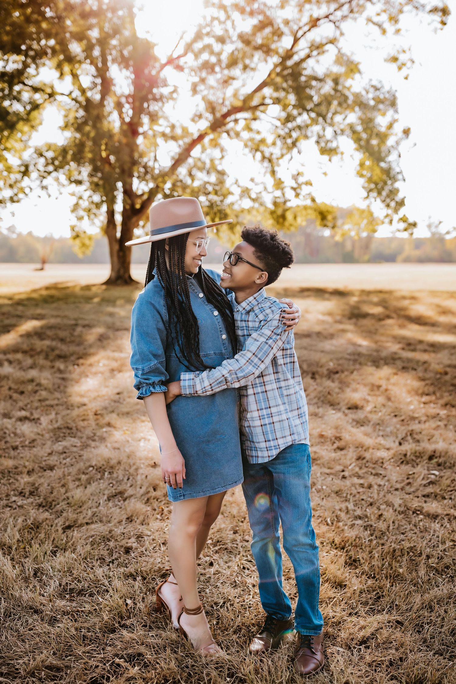 Couple embracing in golden sunset field wearing casual denim outfits.