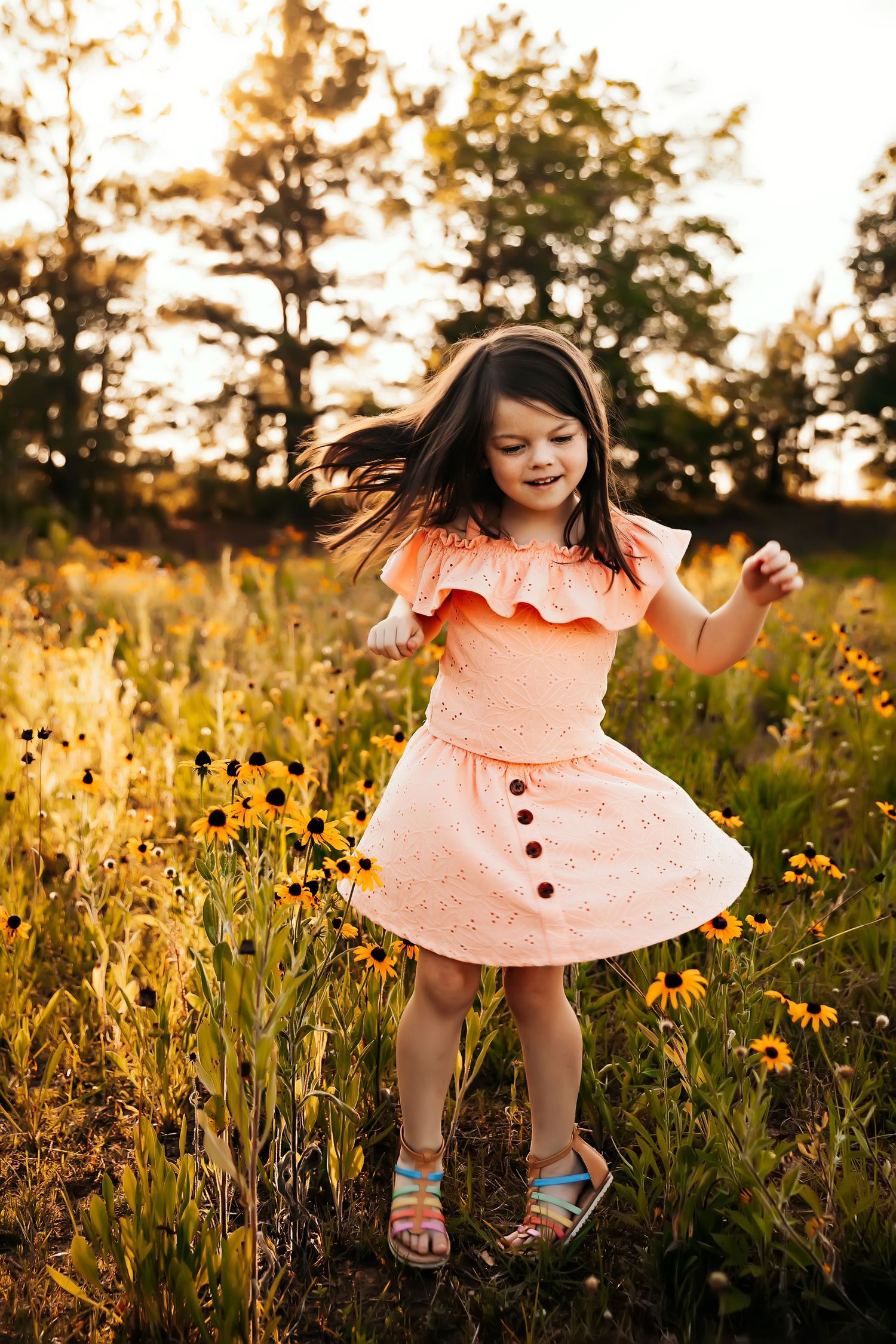 Young dancer in peach ruffled dress twirls among wildflowers at sunset.