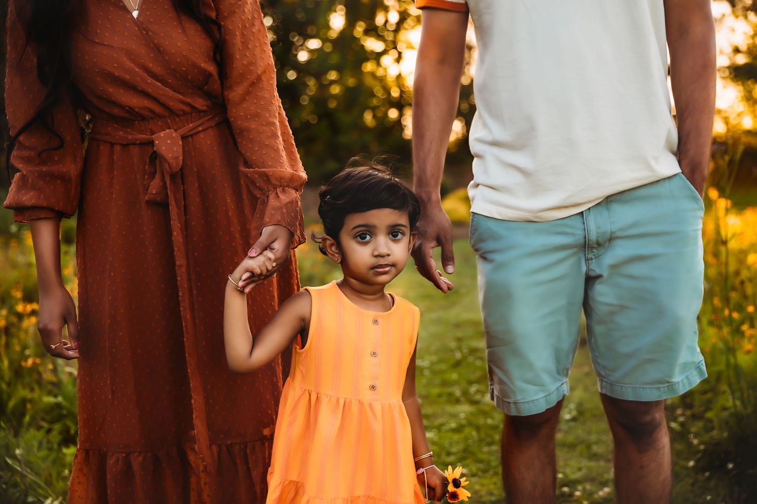 A family walks together at sunset wearing casual clothing in a grassy field.