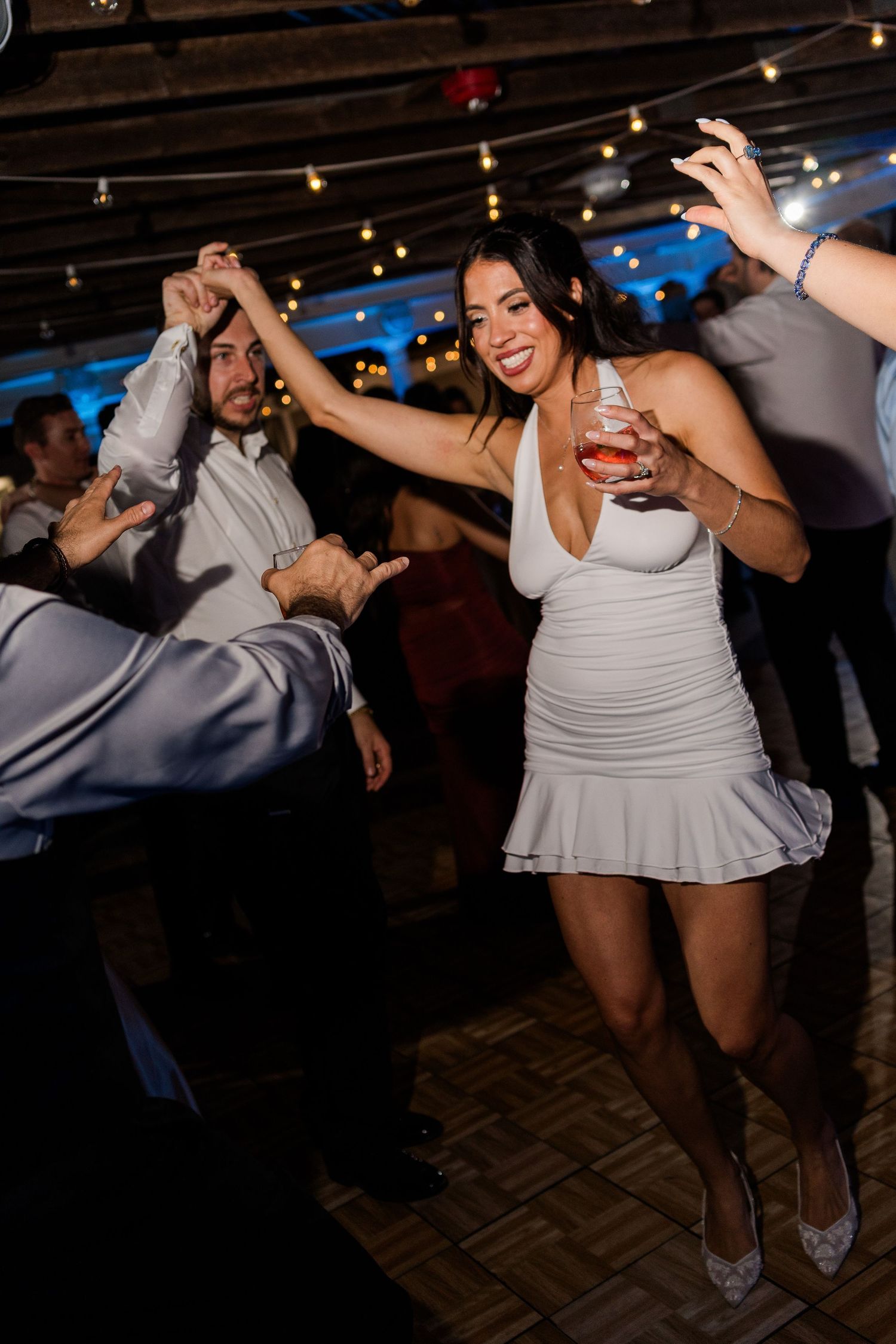 Woman in white dress dancing and holding a drink at an elegant wedding reception party.