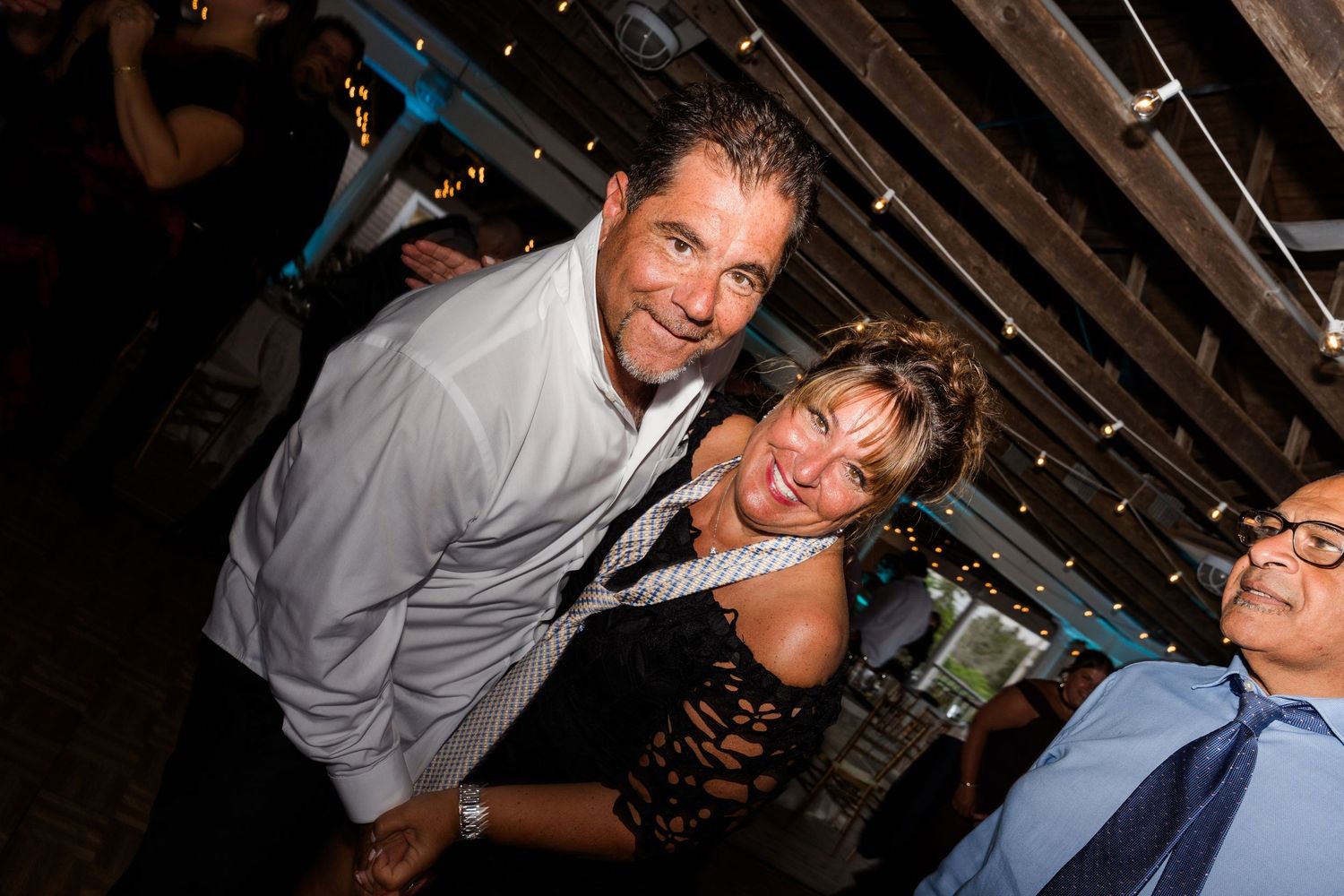 Man and woman smiling and posing together at a lively indoor party or event.