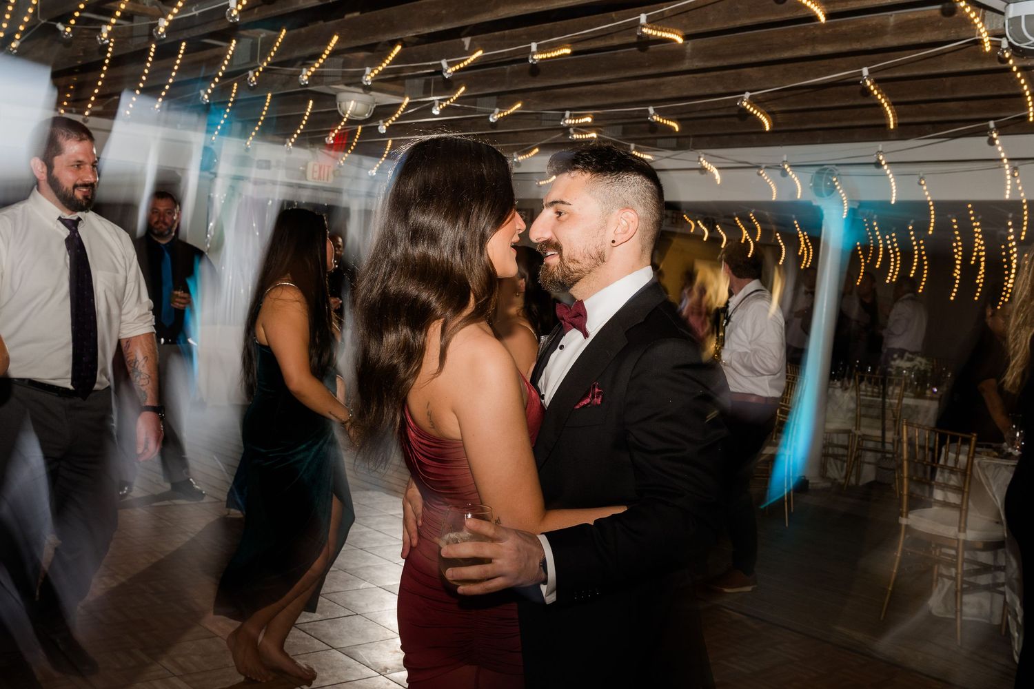 Couple sharing a romantic dance at a wedding reception with warm string lights in the background.