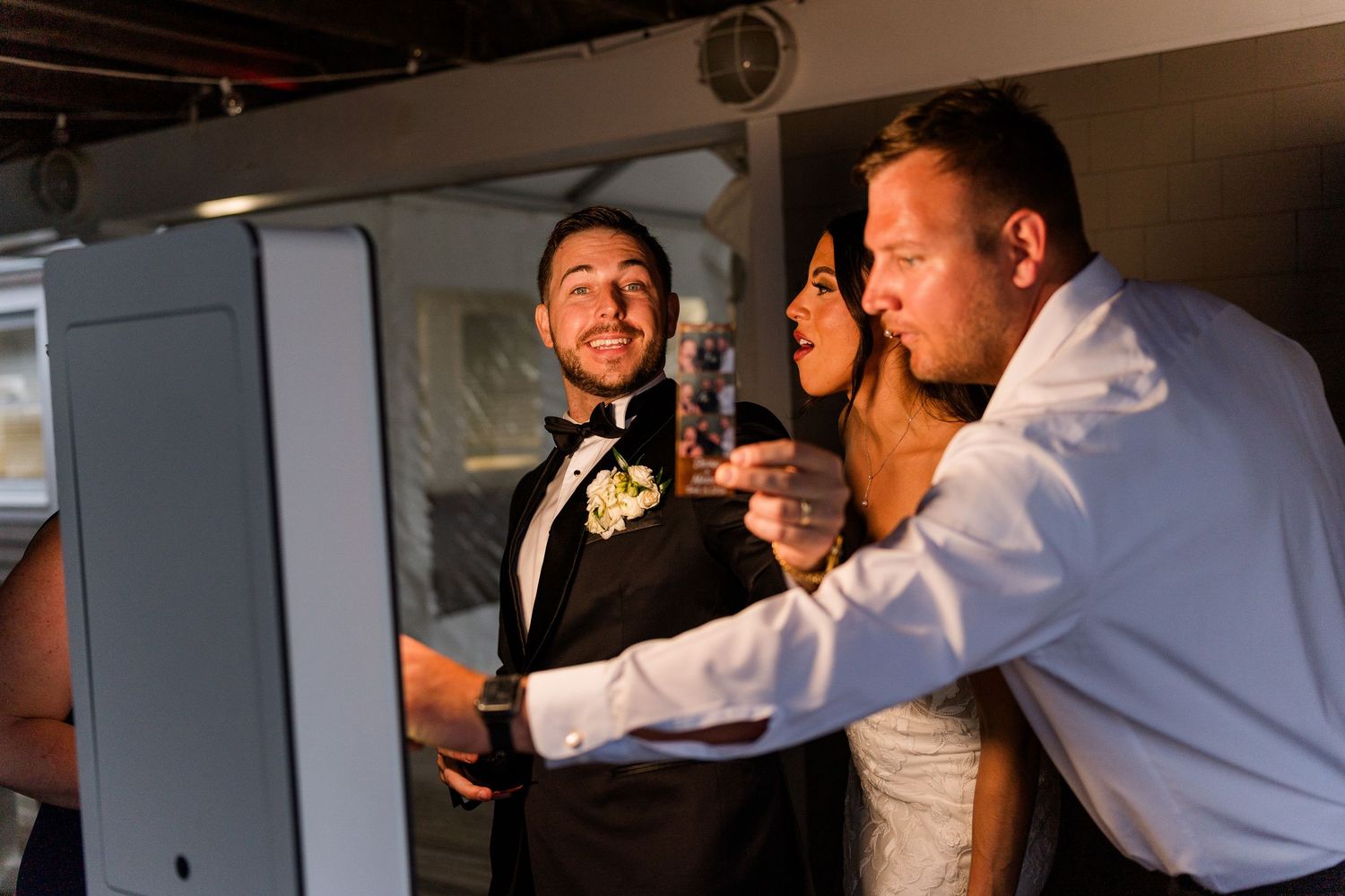 Bride and groom smile with a guest at a photo booth during their wedding reception.