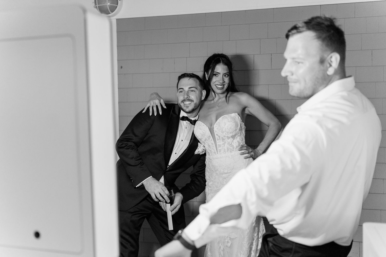 Black and white wedding photo of bride and groom posing with a guest in formal attire.