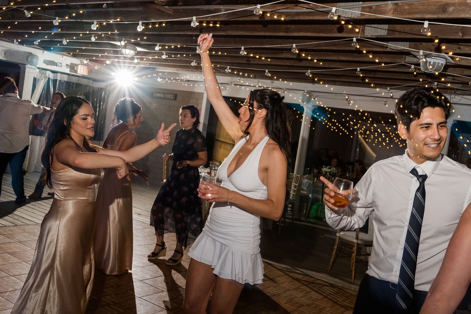 Guests dancing joyfully at an outdoor wedding reception with string lights overhead.