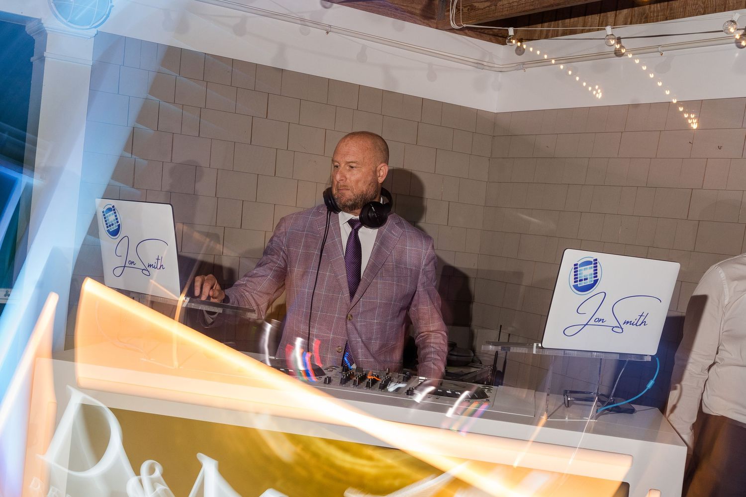 DJ mixing music at a wedding reception behind a professional setup in a stylish venue.