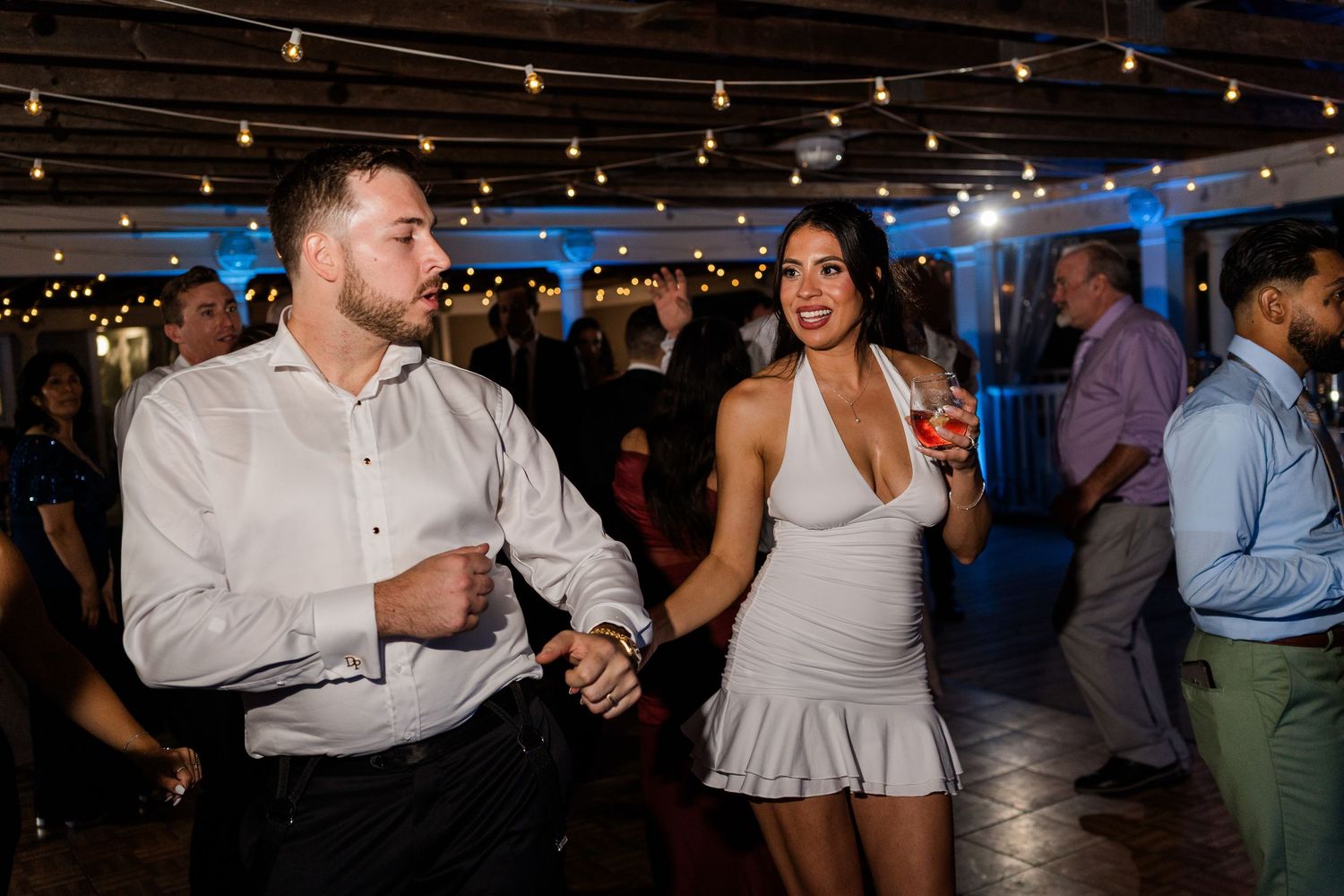 Couple dances together at a festive wedding reception with string lights and blue lighting.