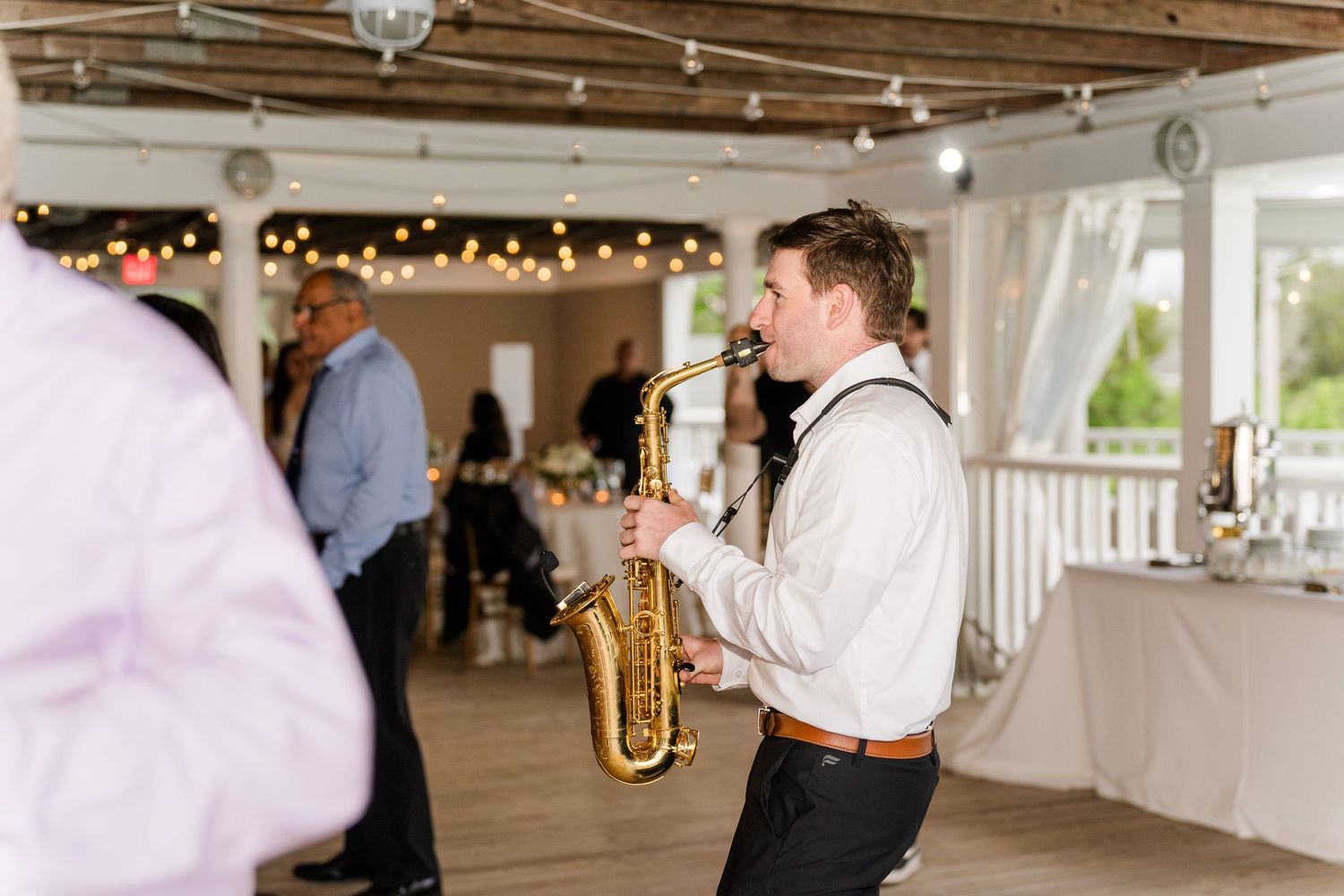 Saxophonist performing live at an elegant wedding reception with string lights and draped curtains.